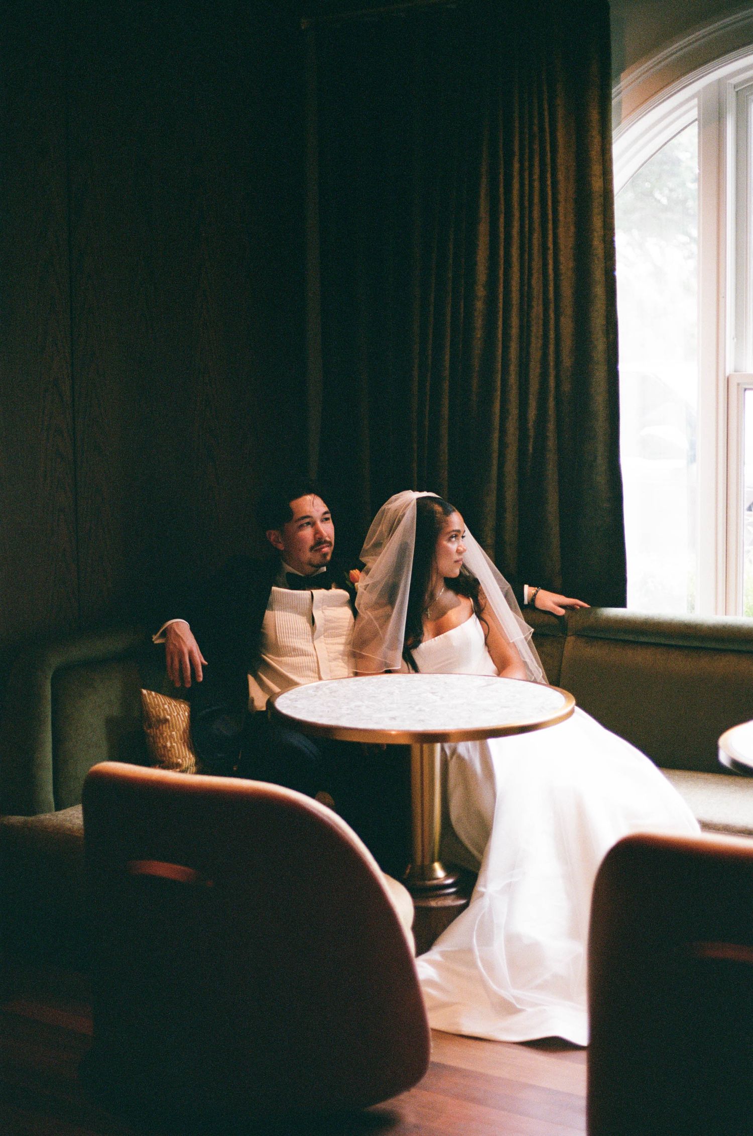 Intimate indoor wedding scene with dramatic lighting and figures seated at a round table.
