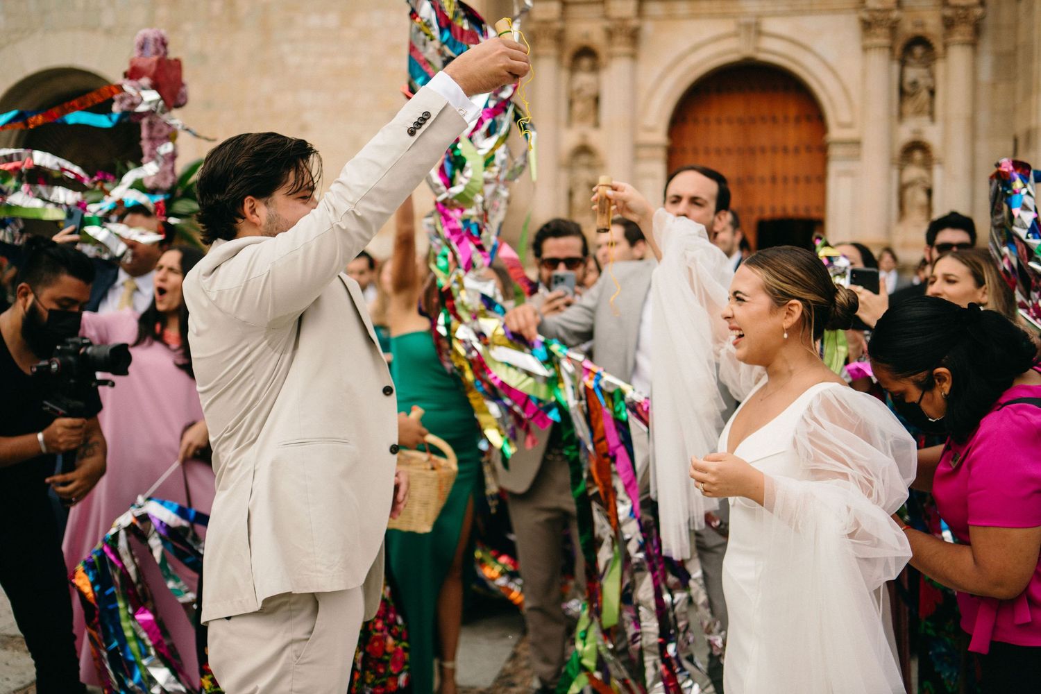 Wedding celebration with guests throwing colorful confetti in front of historic building.