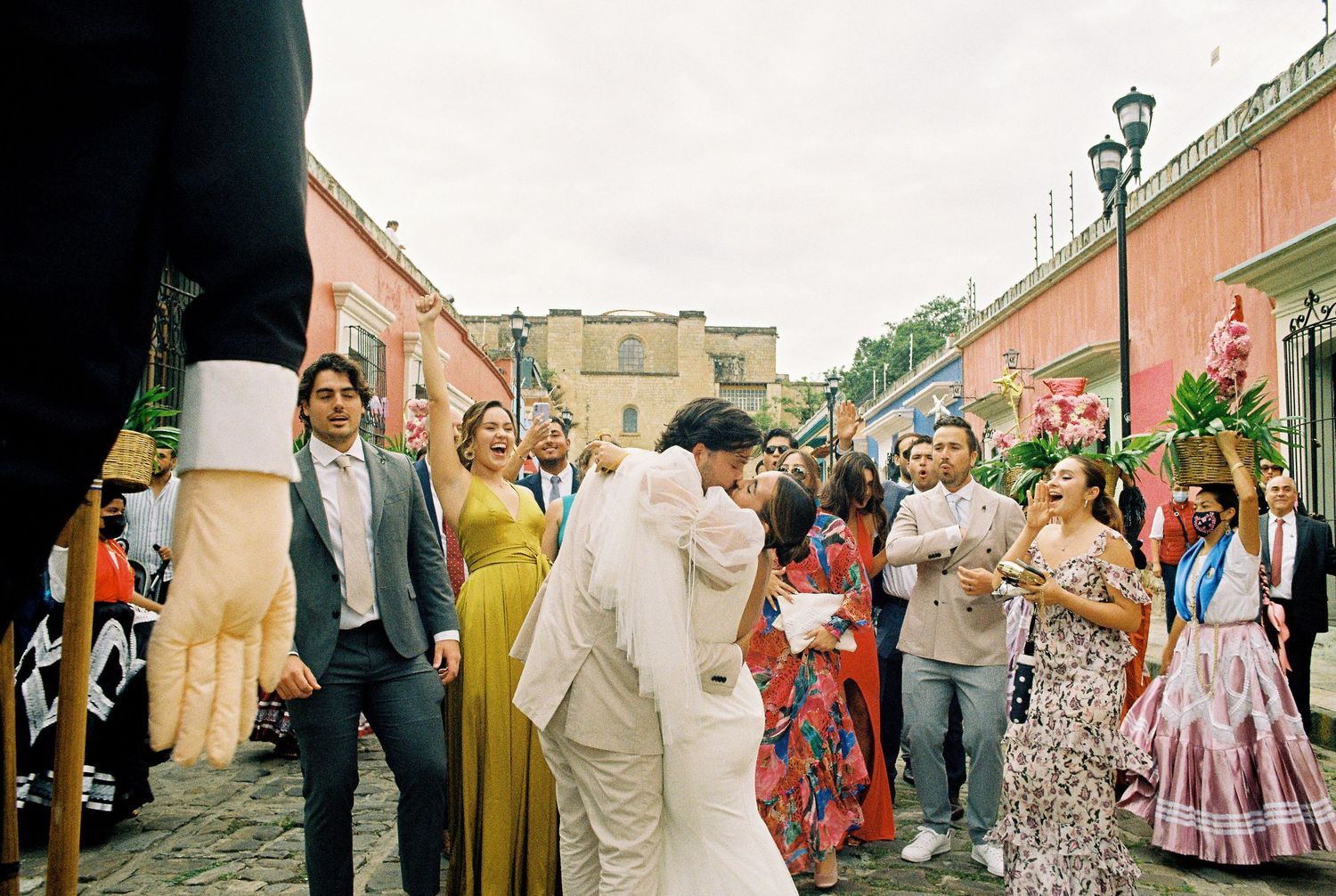 Street celebration with dancers and onlookers along colorful colonial architecture.