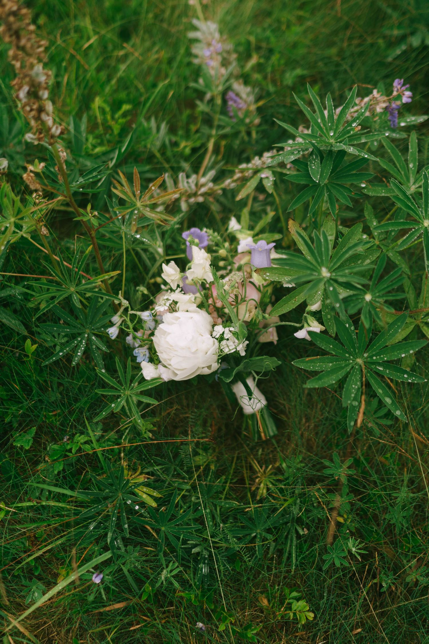 White floral bouquet rests in green grass and foliage.