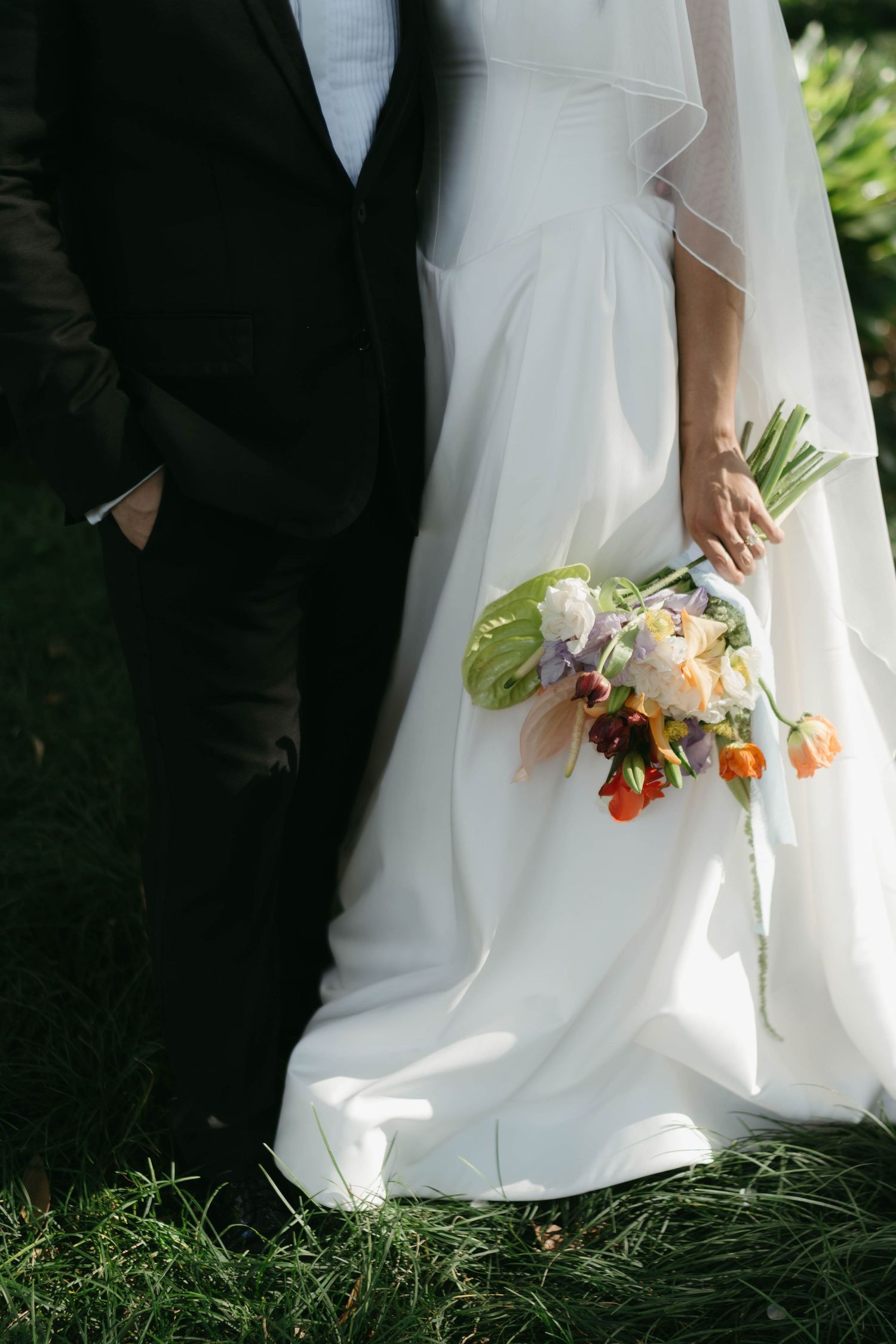 Close-up of wedding dress and bouquet details against green grass.