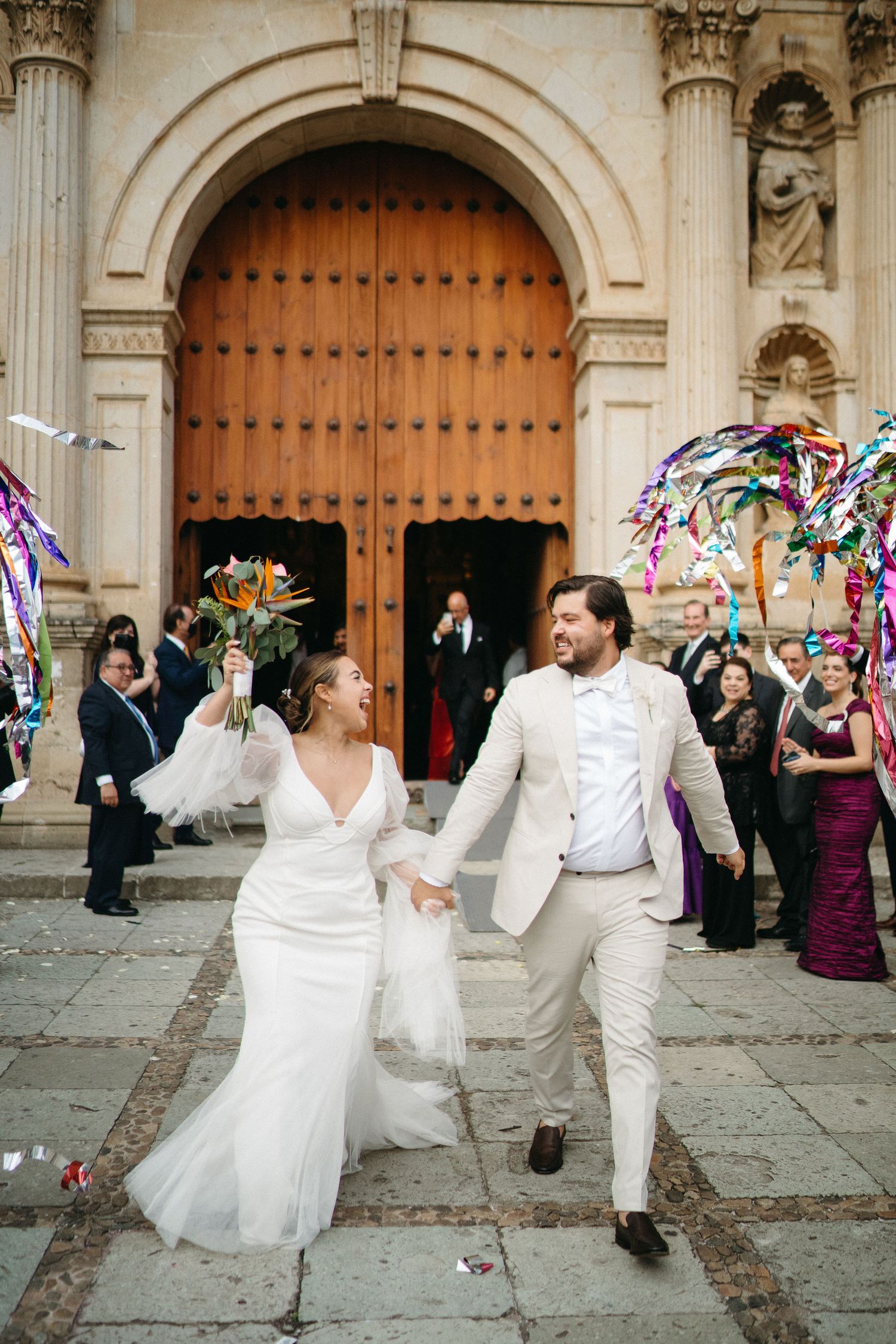 A joyful wedding celebration outside a historic church with guests throwing colorful streamers and ribbons.
