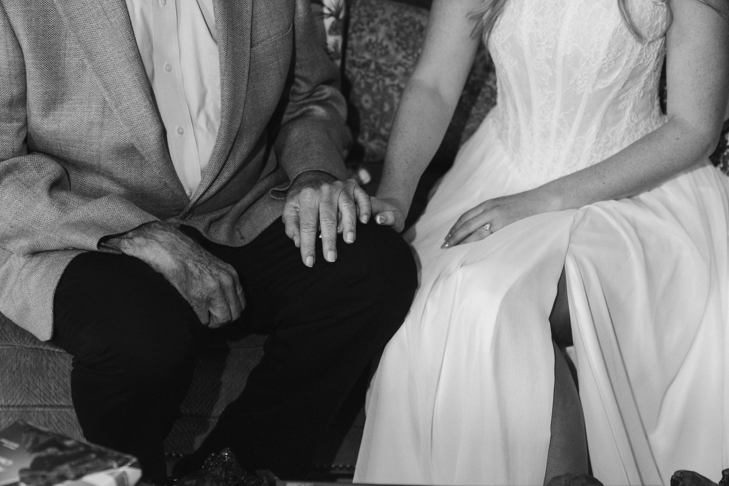 Black and white close-up of bride and groom holding hands while seated together.
