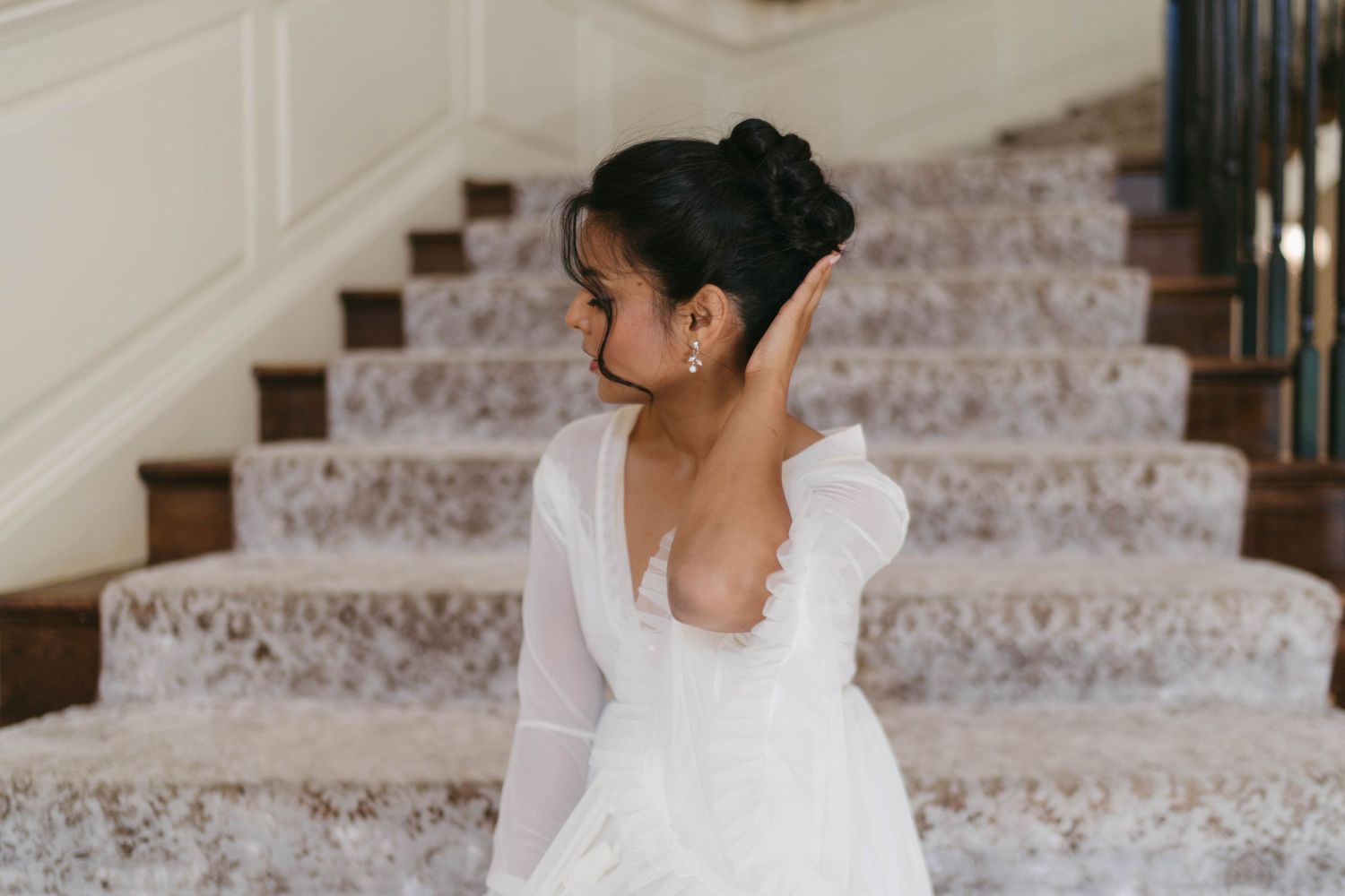 Bride in white gown with puff sleeves and elegant updo poses on carpeted staircase, showing off open back dress.