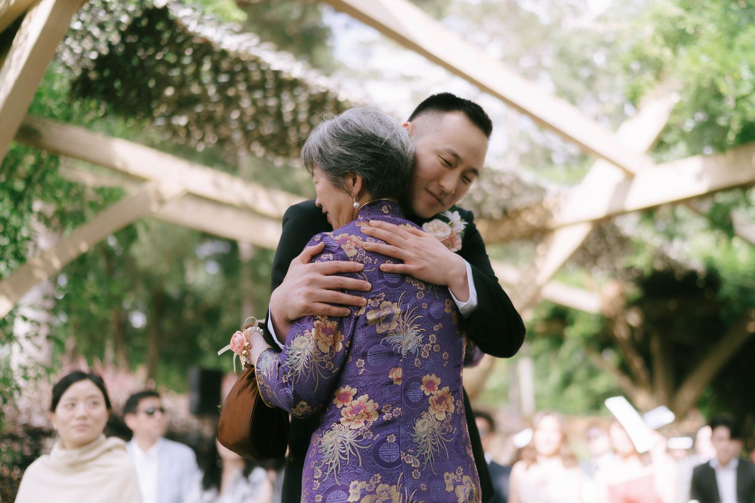 A tender embrace shared during an outdoor wedding celebration under a wooden pergola.