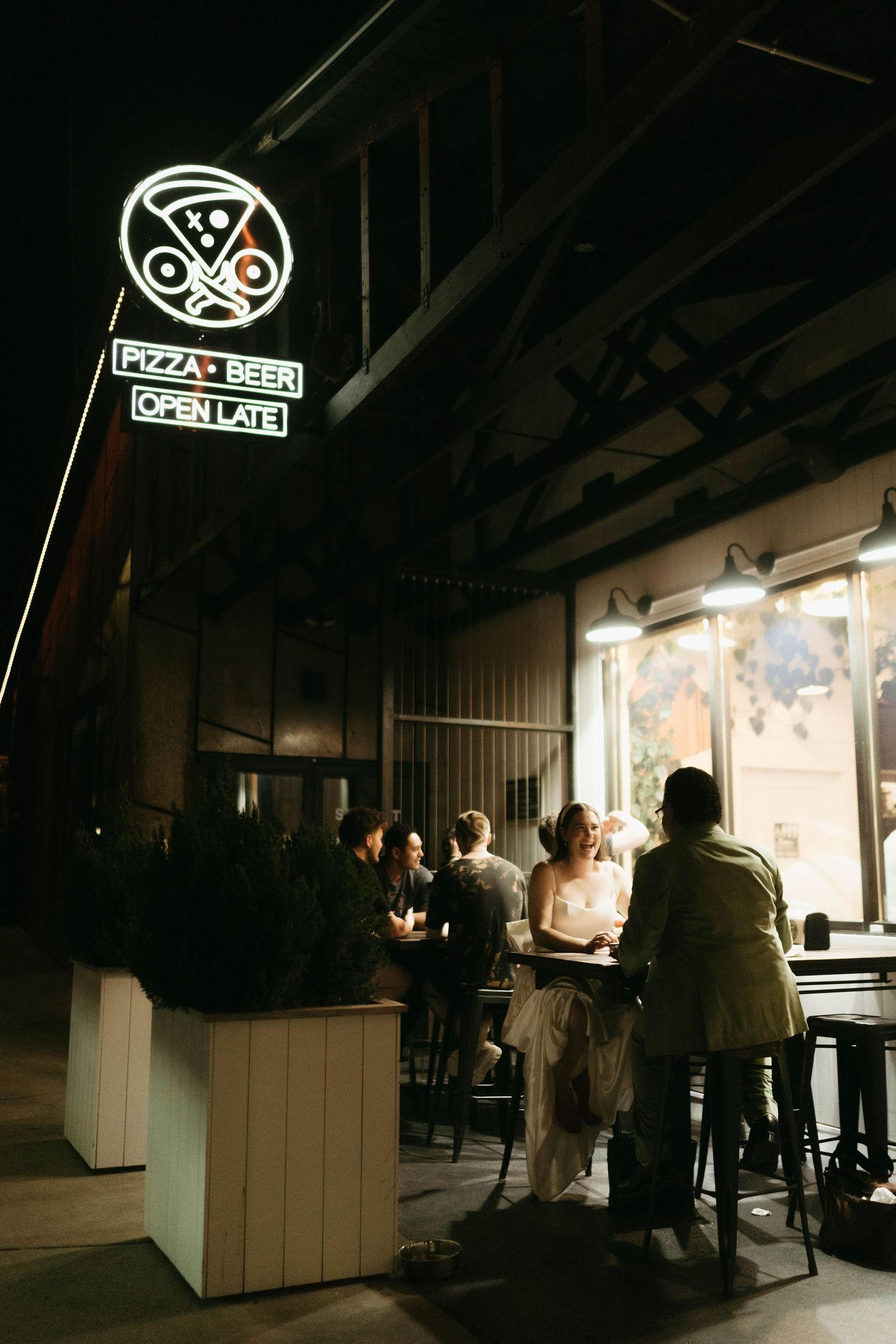 Silhouetted figures in a dark restaurant space with illuminated pizza and beer signage.