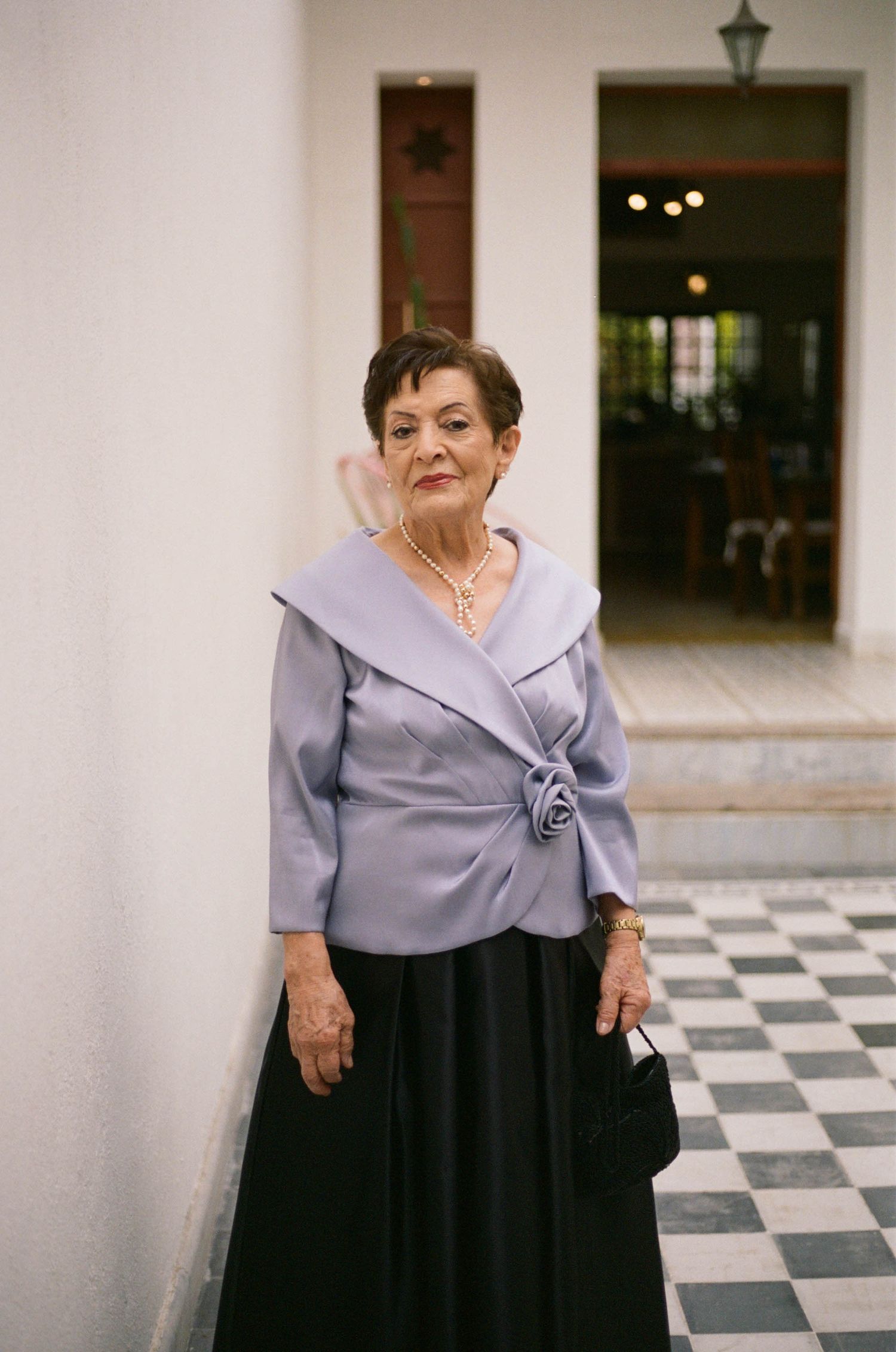 Woman in a lavender blouse and black skirt poses on a checkered floor.