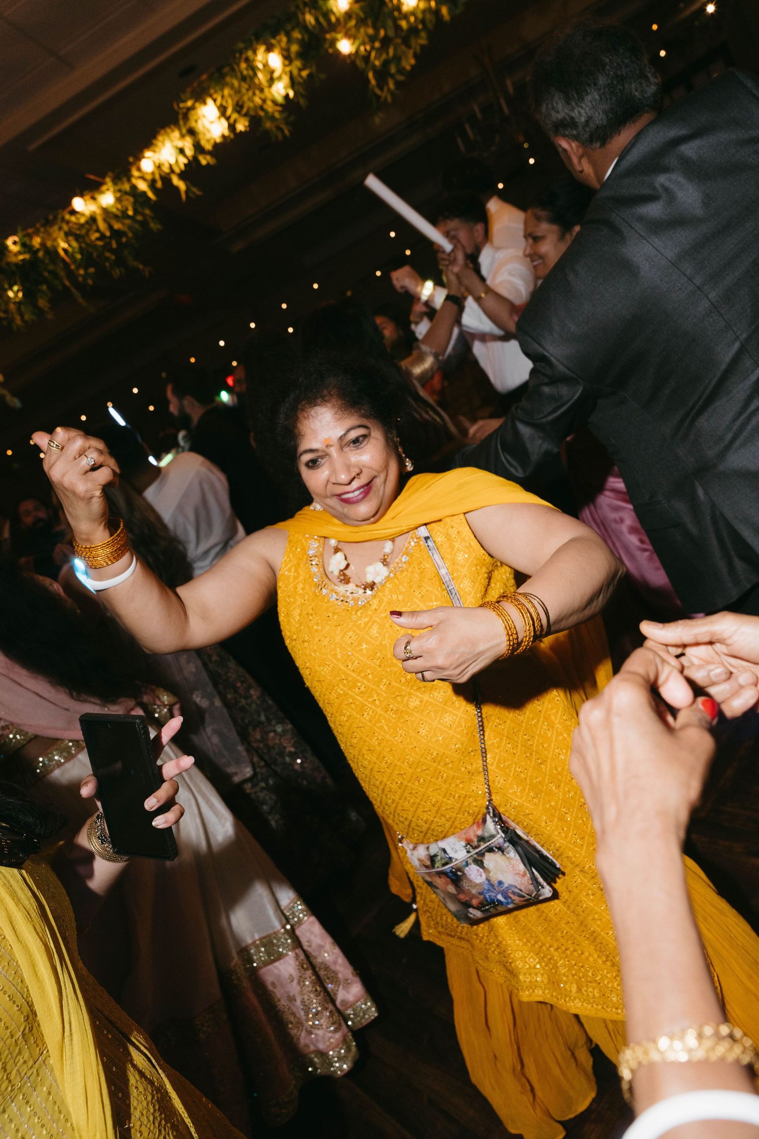 Woman in vibrant yellow salwar kameez dancing joyfully at an Indian wedding reception celebration.