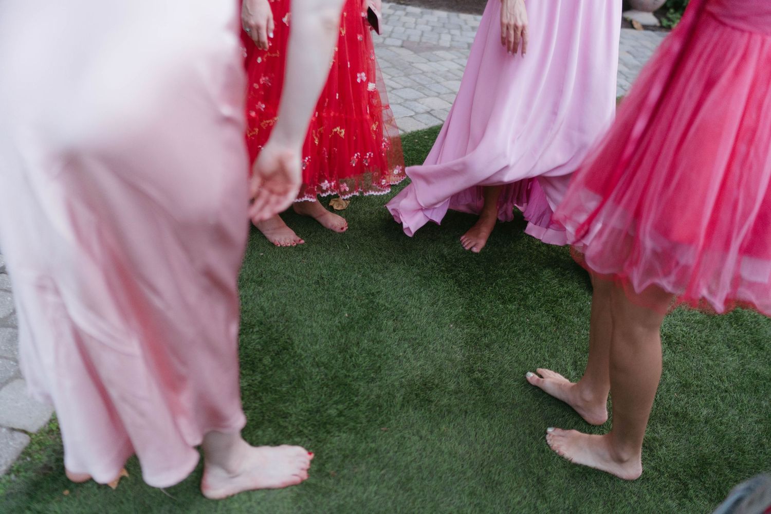 Wedding guests in pink and red dresses dancing on artificial turf at outdoor reception.