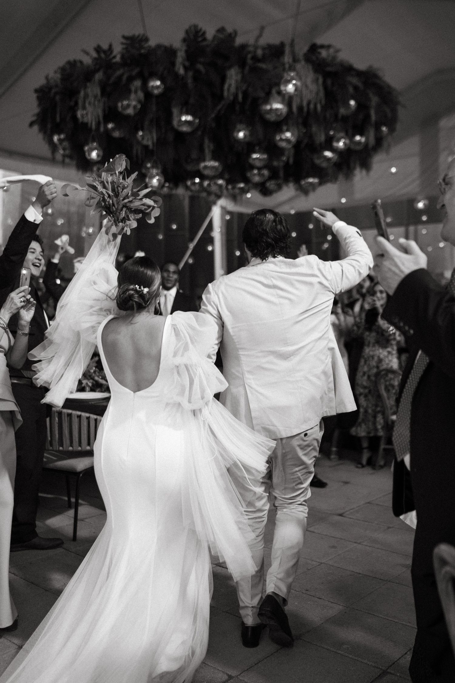 Wedding couple dances in elegant white reception venue with dramatic lighting.