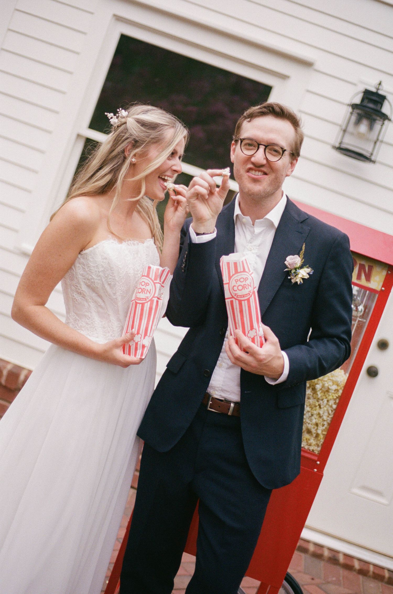 Bride and groom smile while holding popcorn boxes at a fun outdoor wedding celebration.