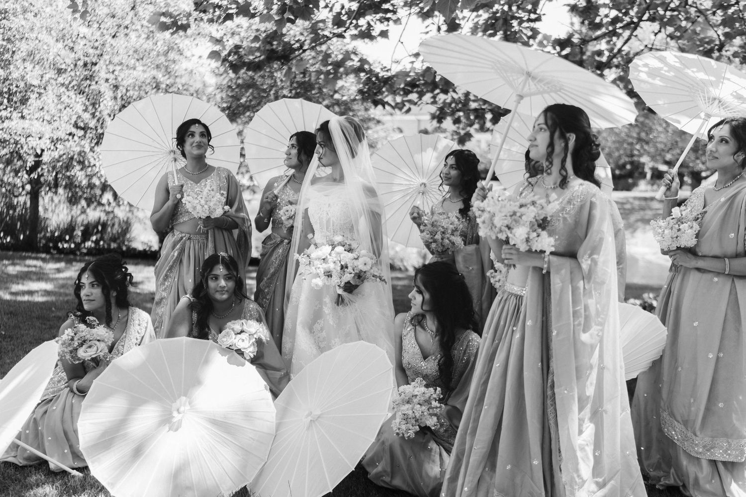 Black and white photo of bride with bridesmaids holding white parasols outdoors.