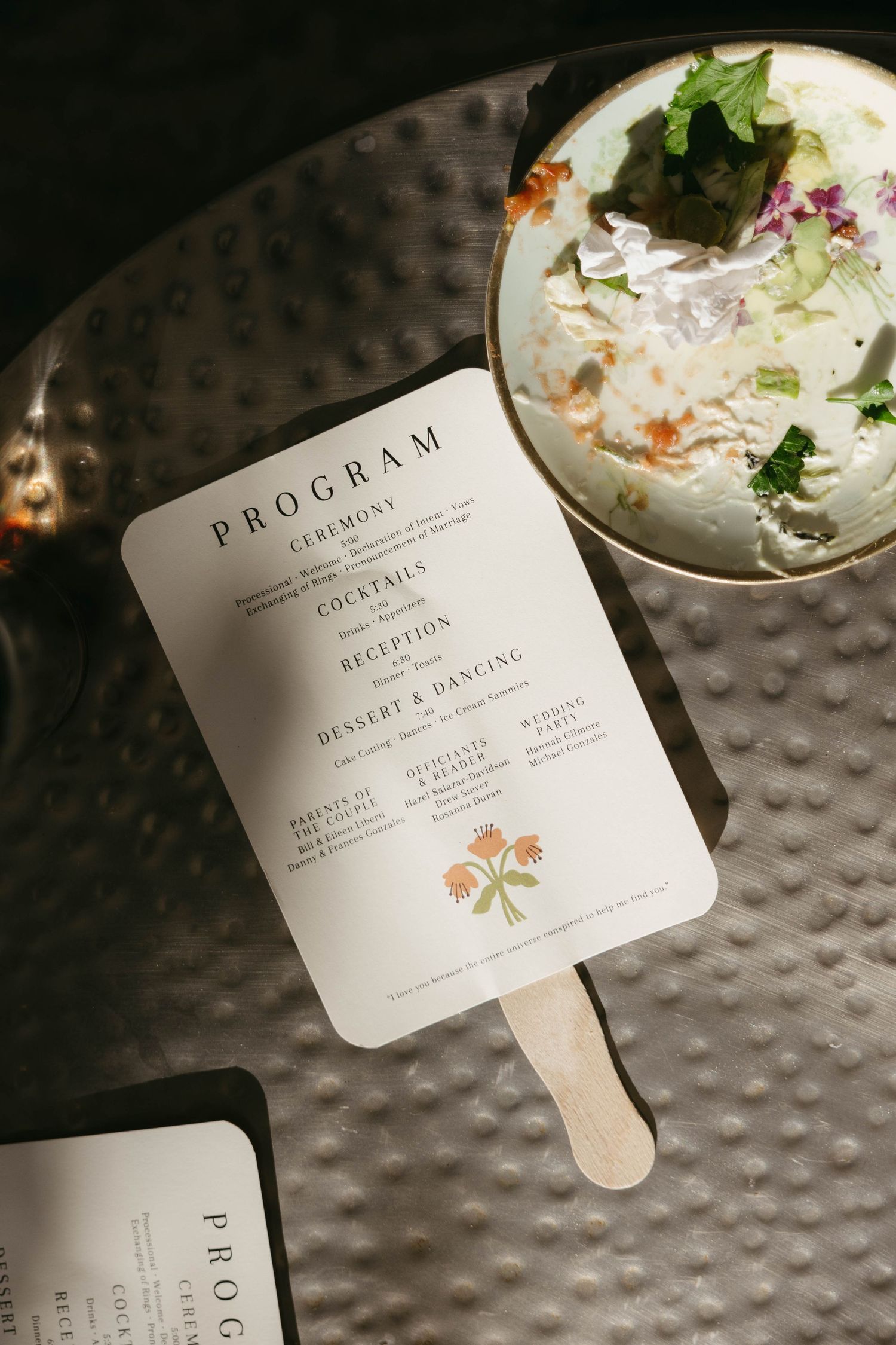 Elegant wedding program fans and menu cards displayed on textured silver surface.