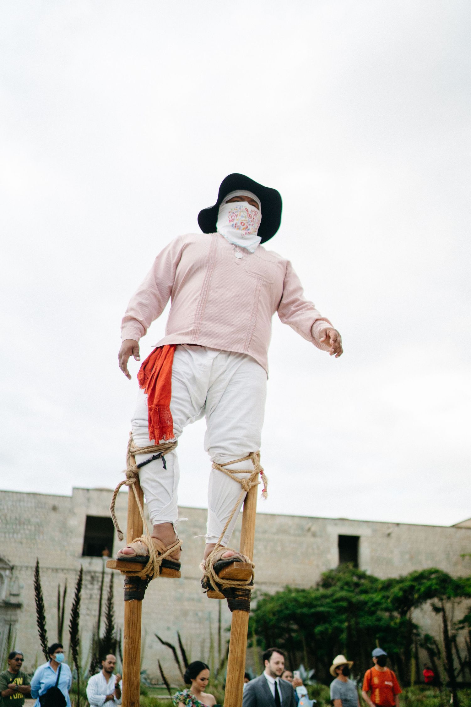 A traditional performer in white pants and pink top balancing on wooden stilts.