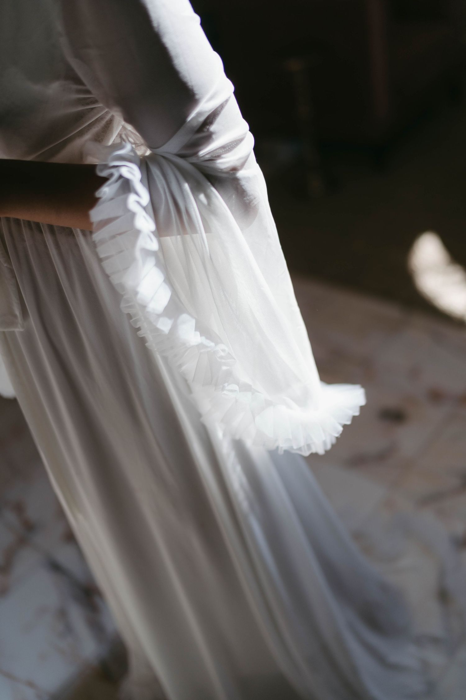 Close-up of a bride's elegant white wedding gown with delicate ruffled tulle details and a satin bow.