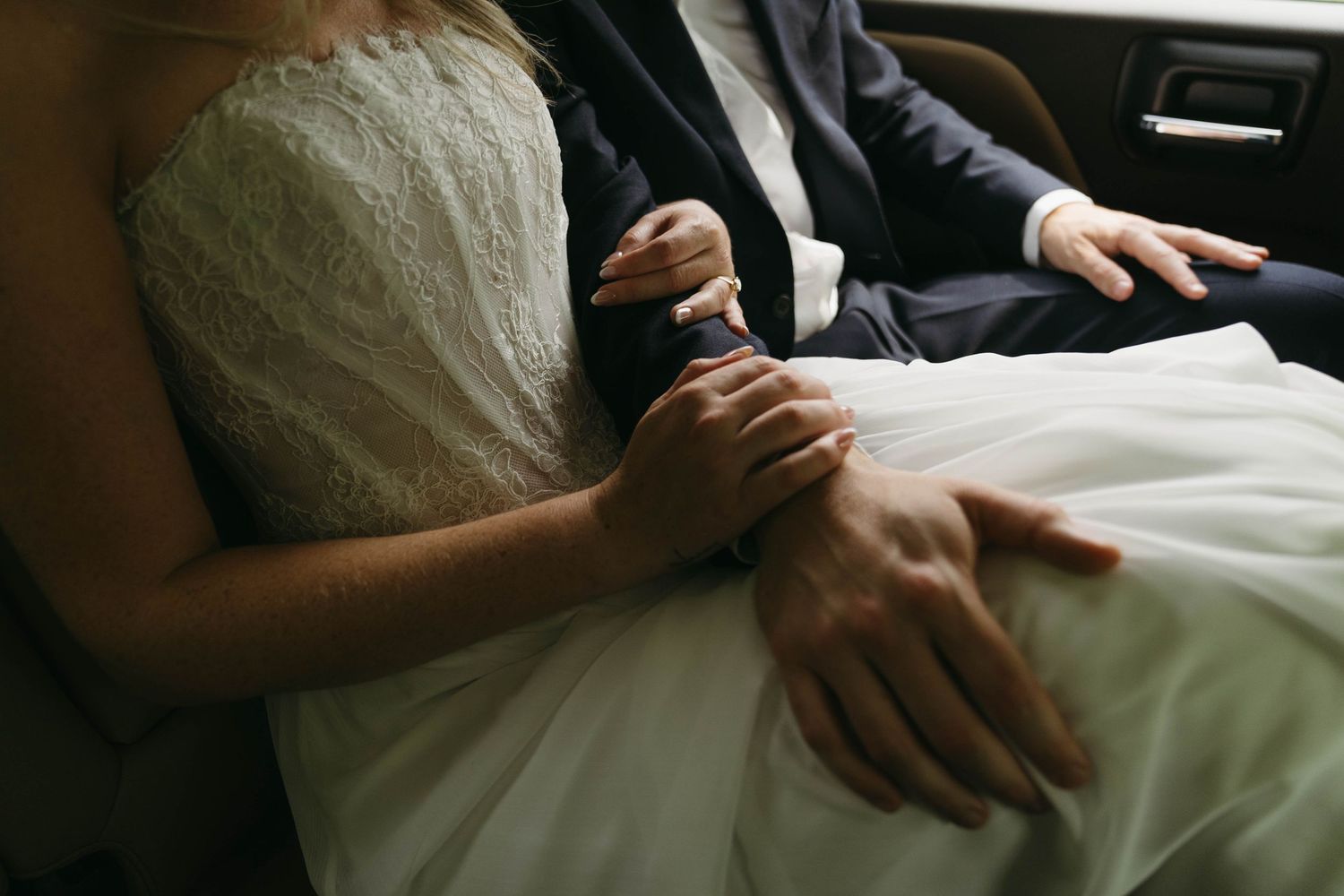 Bride and groom holding hands in lace wedding dress and navy suit.