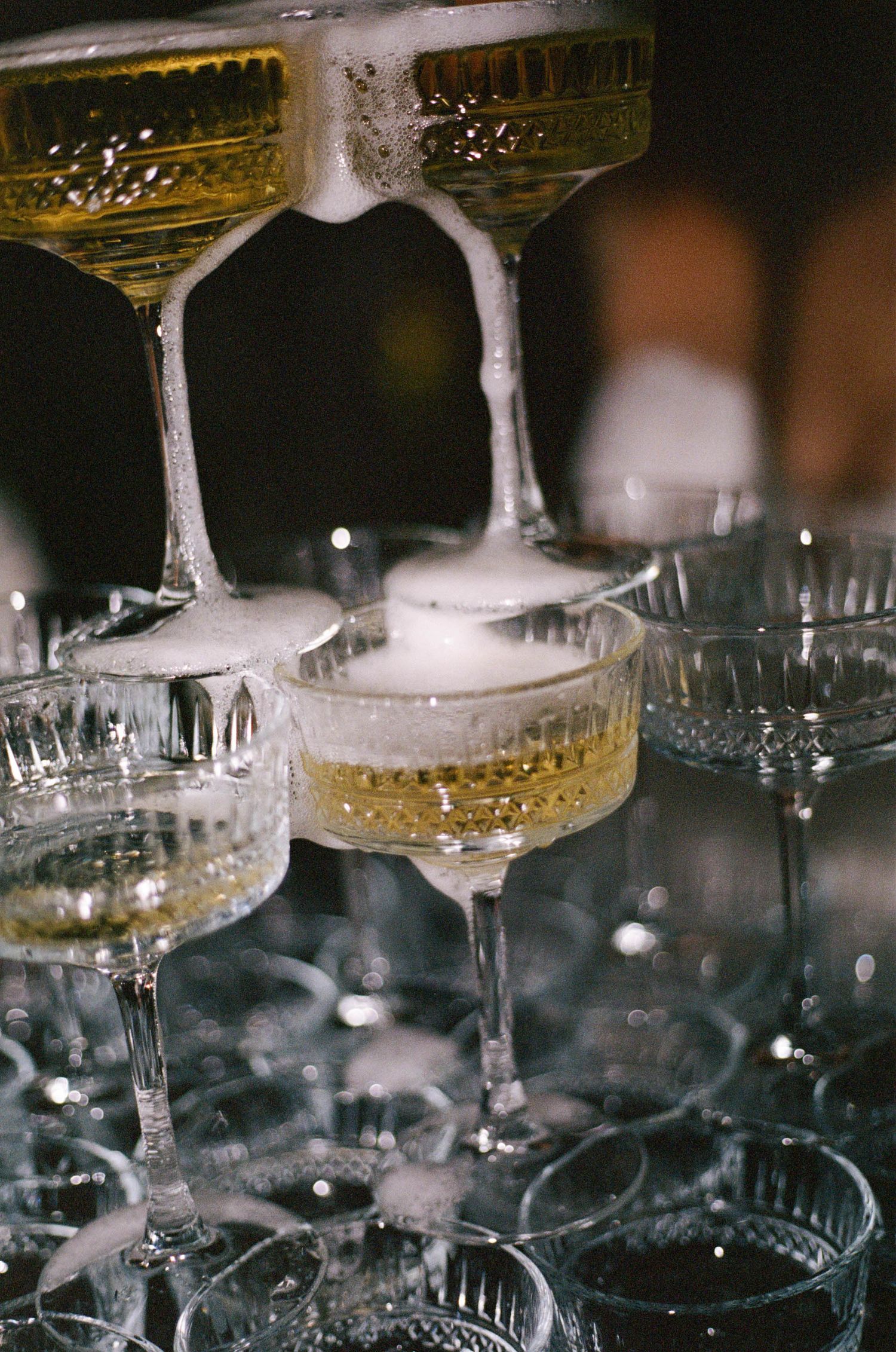 Close-up of champagne flowing through stacked crystal coupe glasses creating a fountain effect.