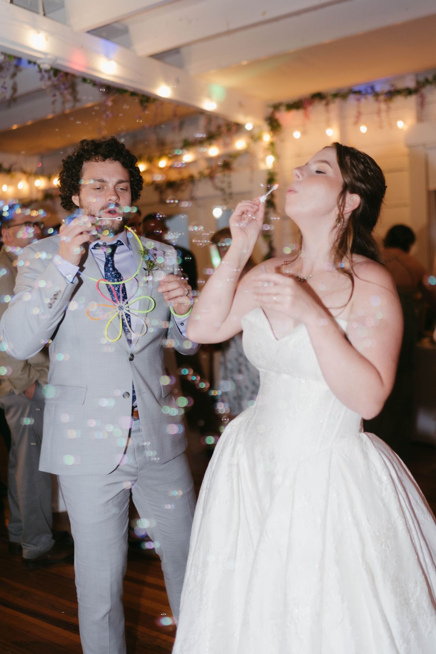Wedding couple shares drinks at indoor reception with sparkling lights and confetti.