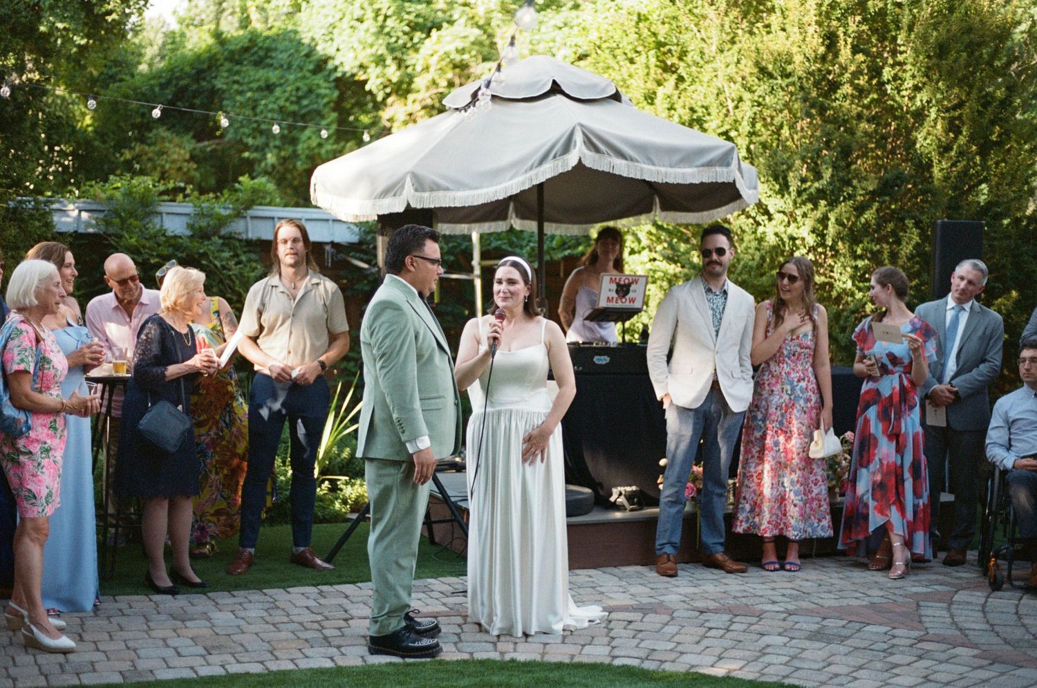 Wedding ceremony under white canopy with guests gathered around brick patio.