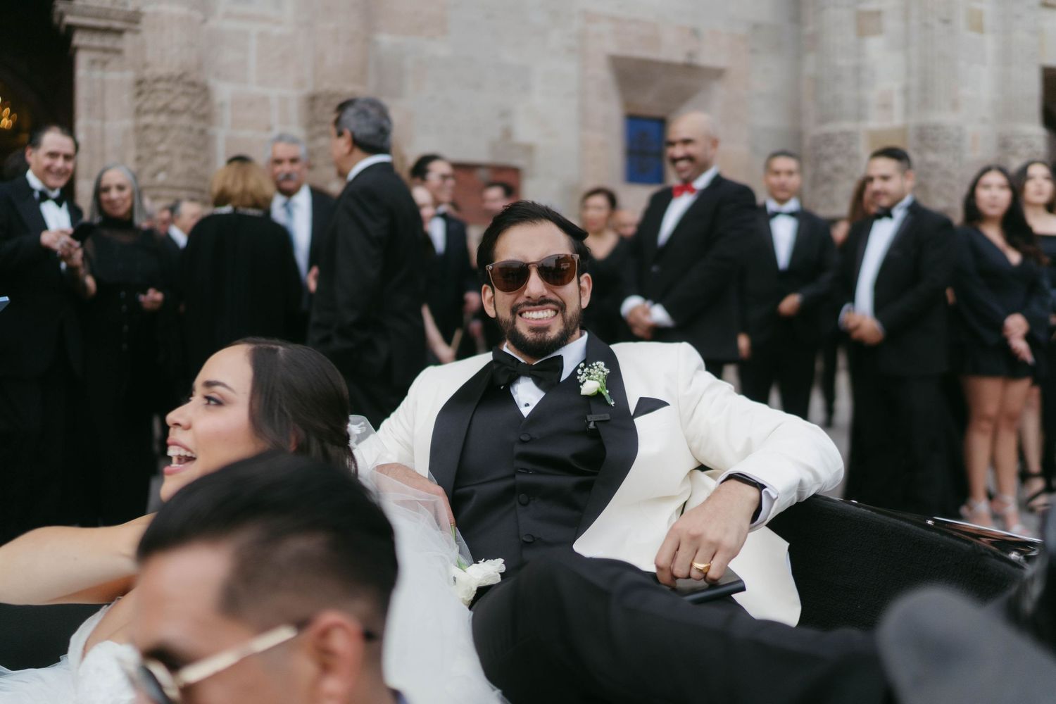 Wedding guests gathered outside a stone building in formal attire.