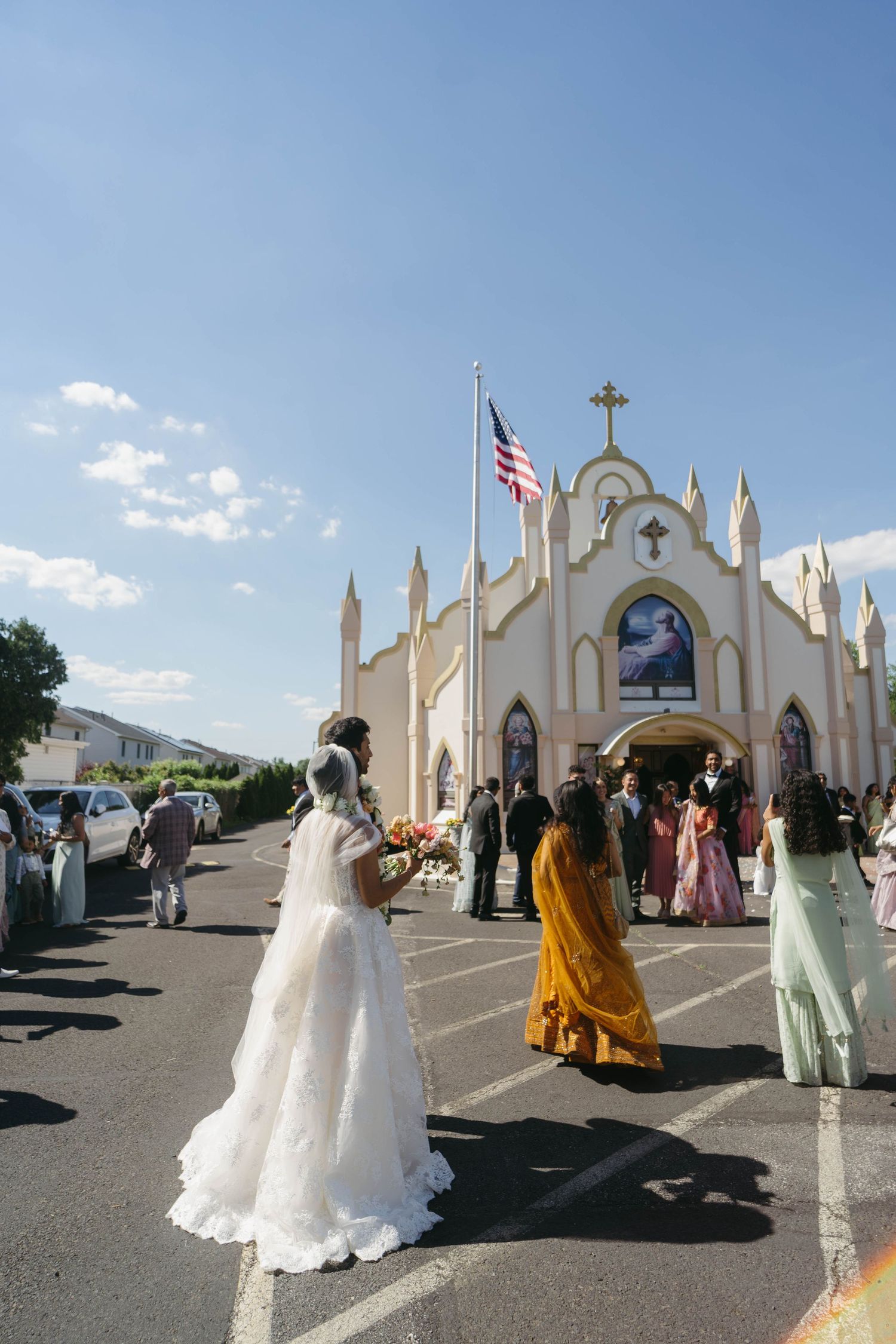 Bride in white gown walks toward a white church with an American flag on her wedding day.