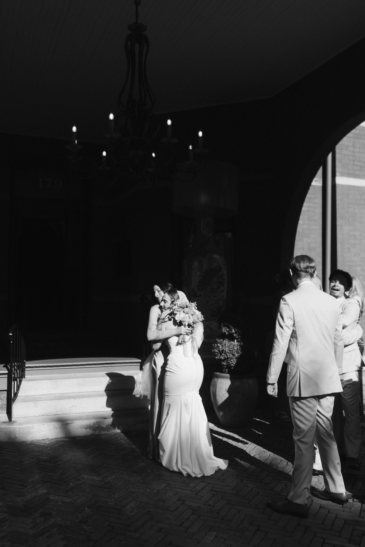 A dramatic black and white wedding photo captured under an elegant chandelier.