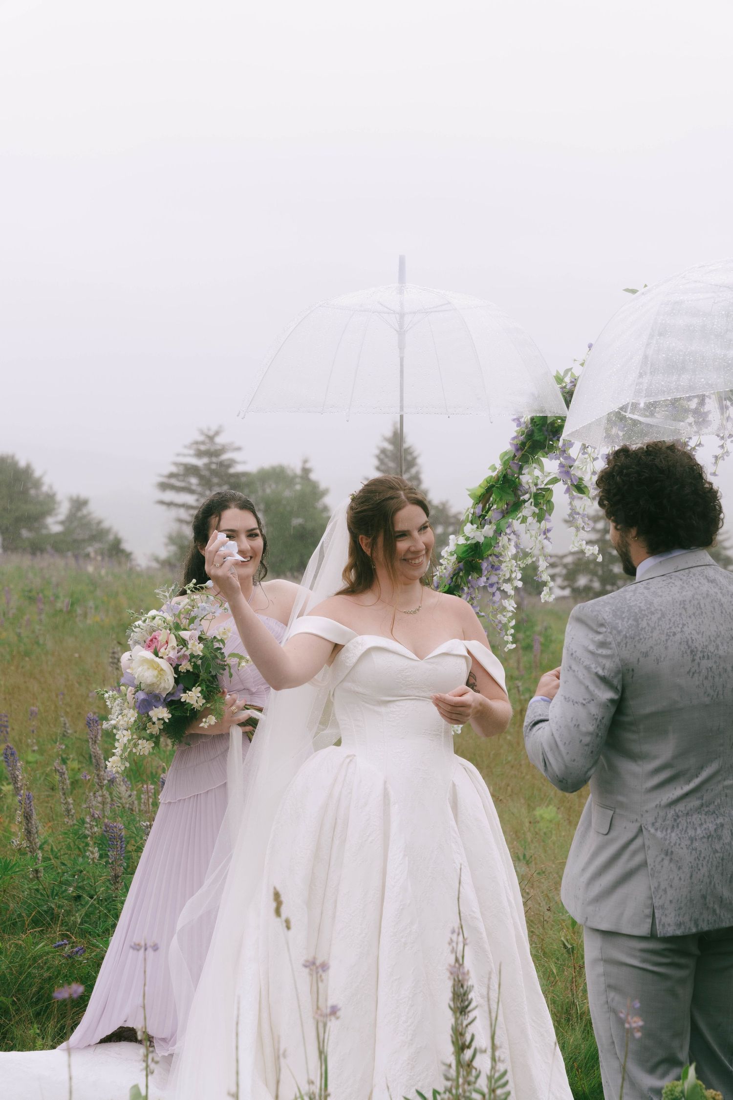 A wedding ceremony takes place under a decorated arch with white fabric and greenery.