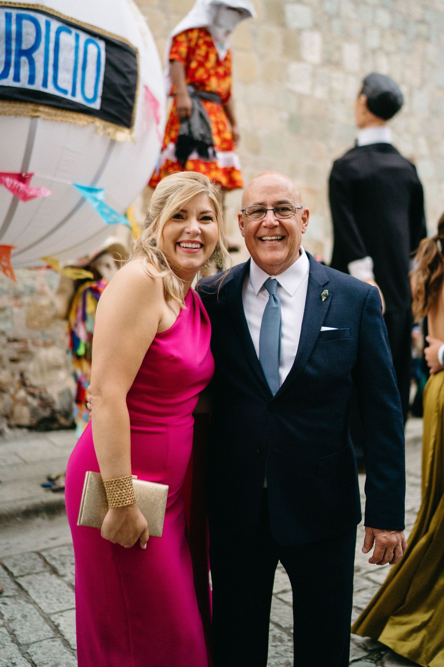 Couple in formal attire smiles and walks together during outdoor celebration.