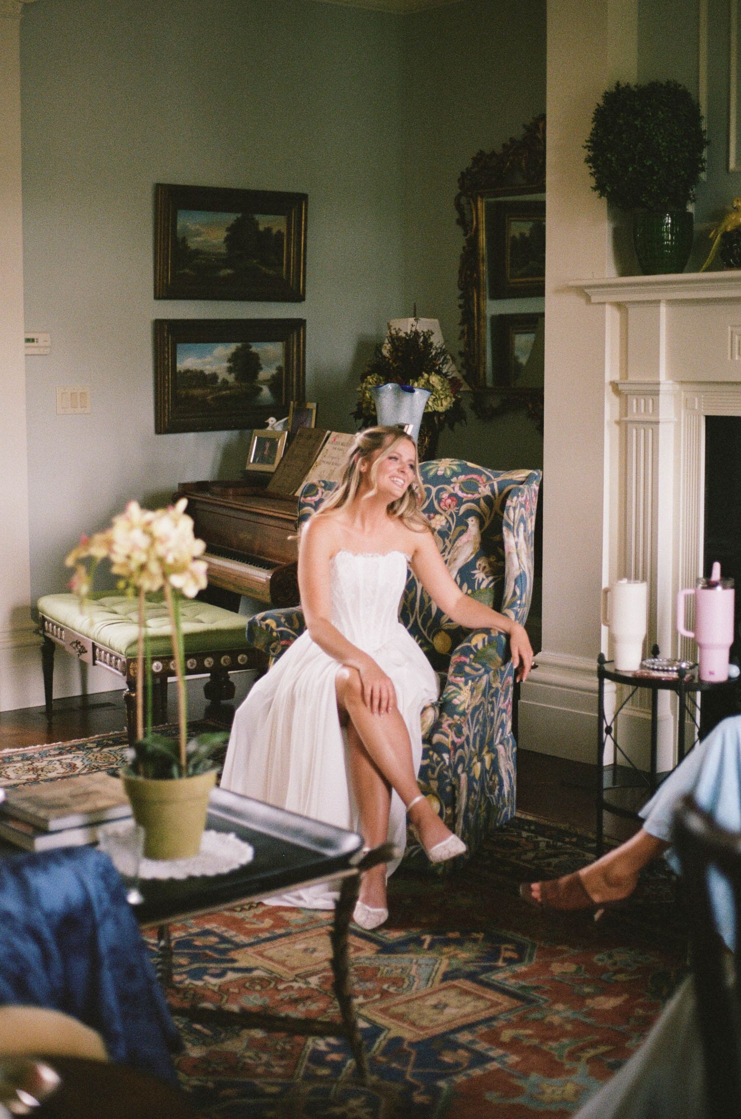 Bride in a white strapless gown sitting in a floral armchair in an elegant vintage-styled room.