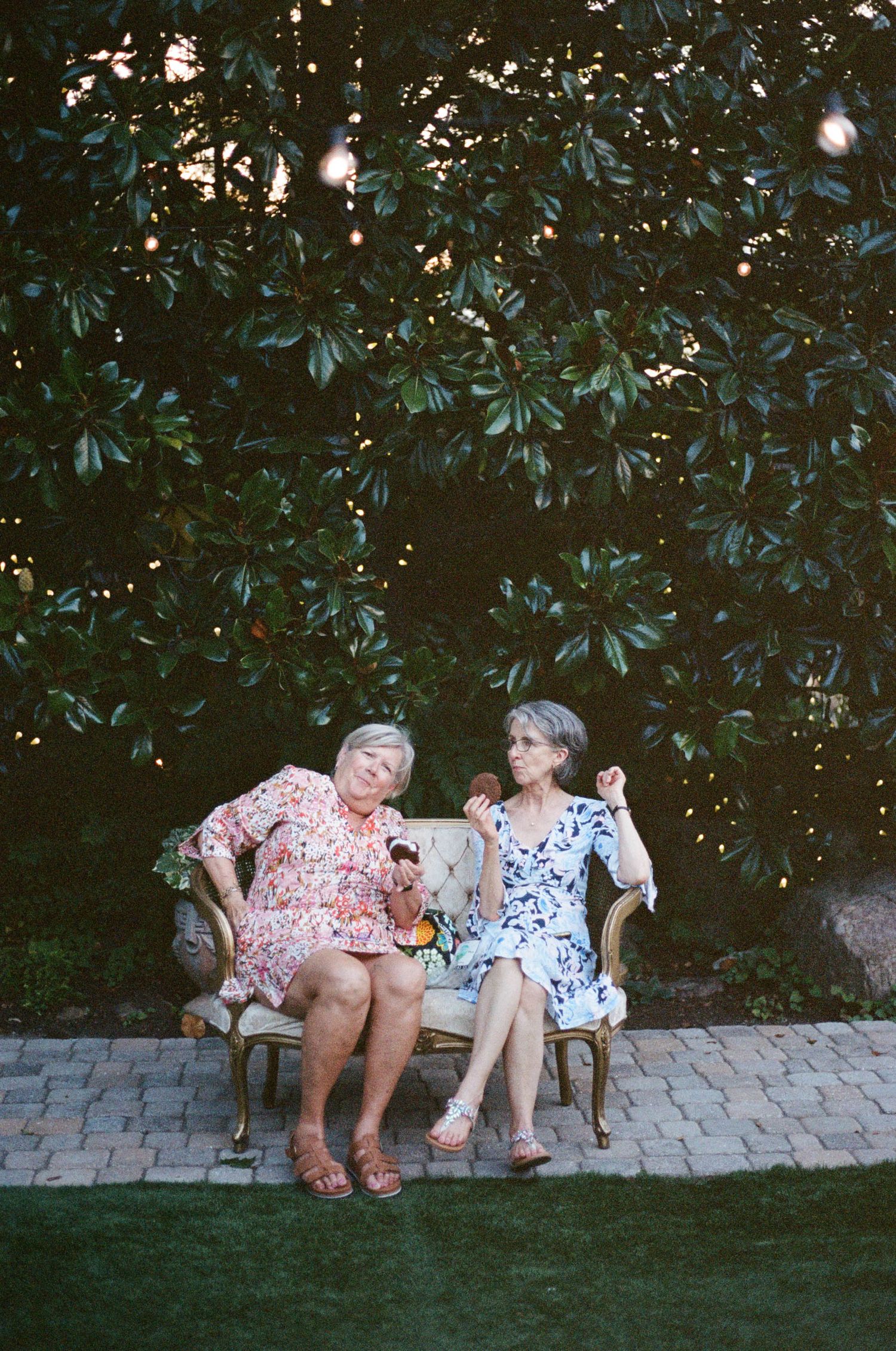 Two guests enjoying refreshments on a garden bench during an outdoor event.