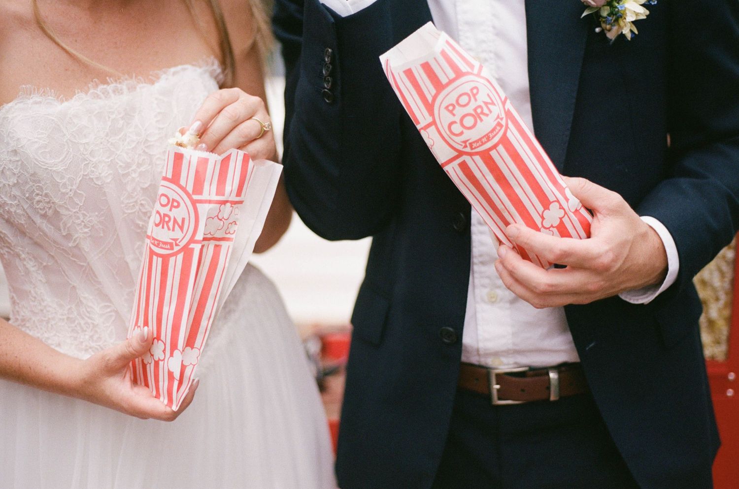 Bride and groom holding red and white striped popcorn bags at outdoor wedding celebration.