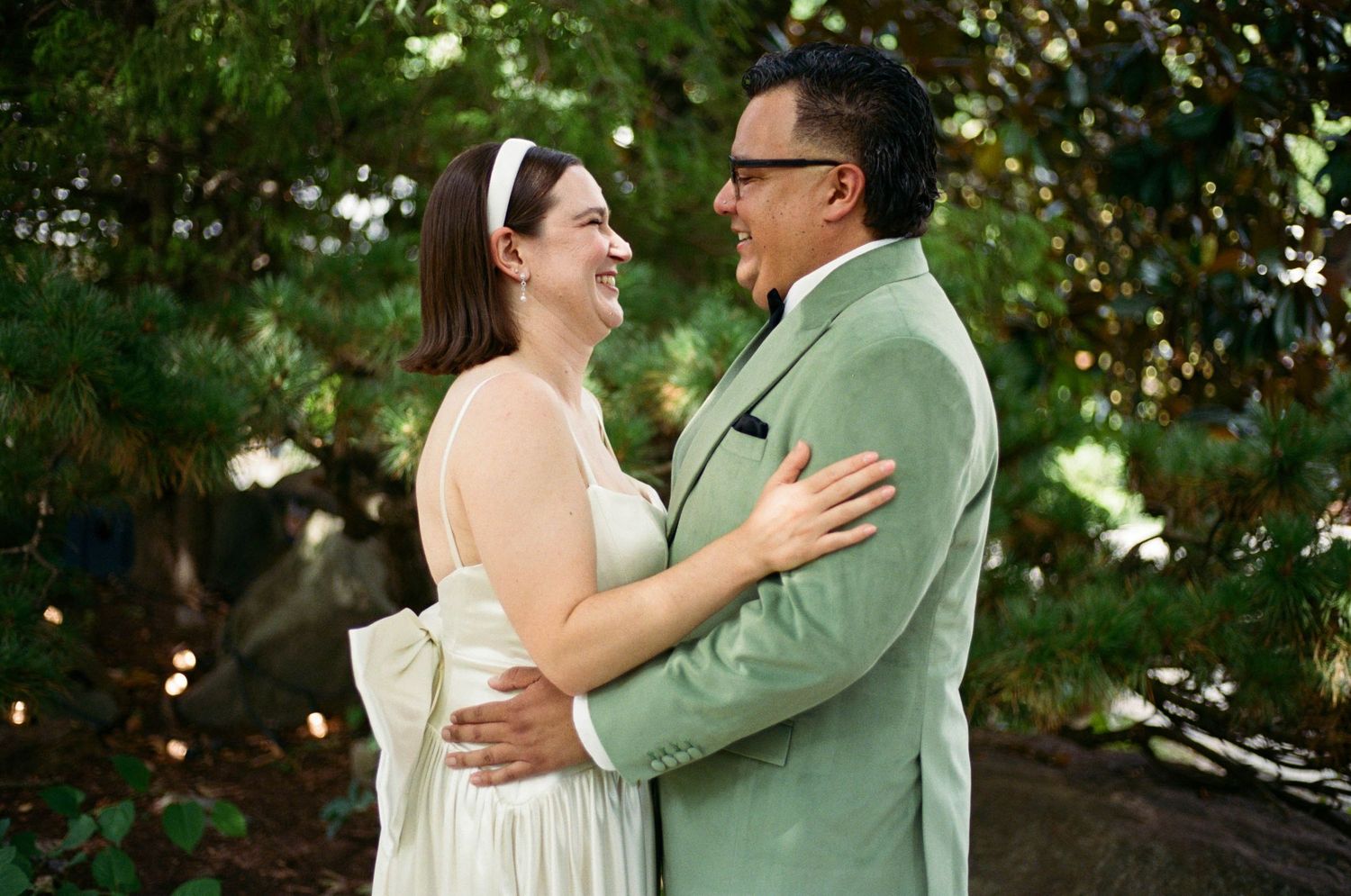 Couple embracing outdoors with one wearing mint green suit and other in cream dress.