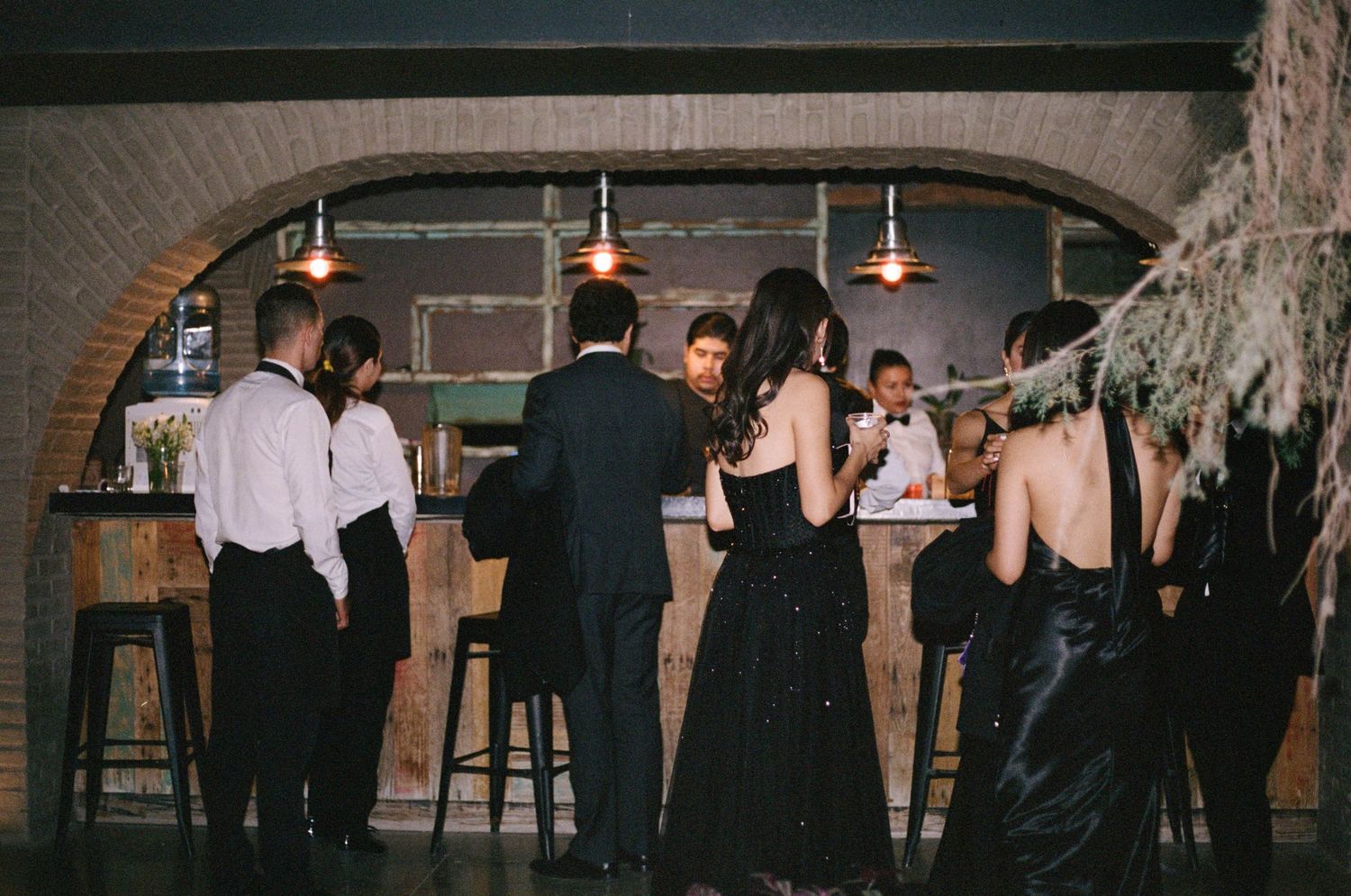 People gathered at a dimly lit bar area with brick archway and ambient lighting.