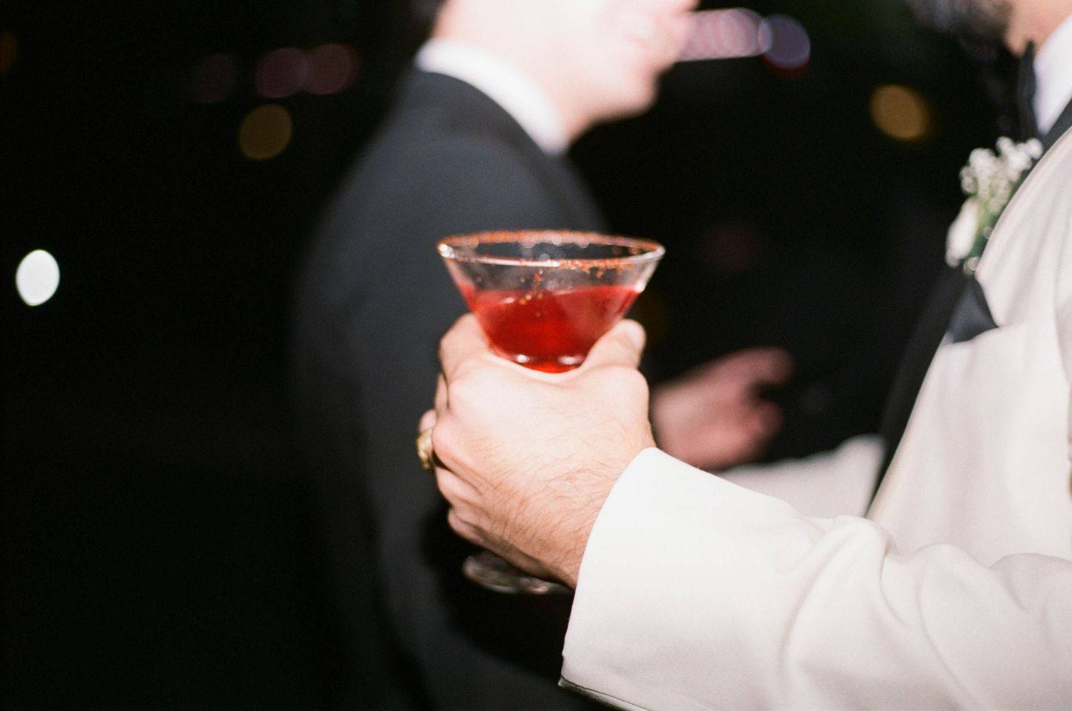 A hand holding a cocktail glass with a red drink against a dark background.