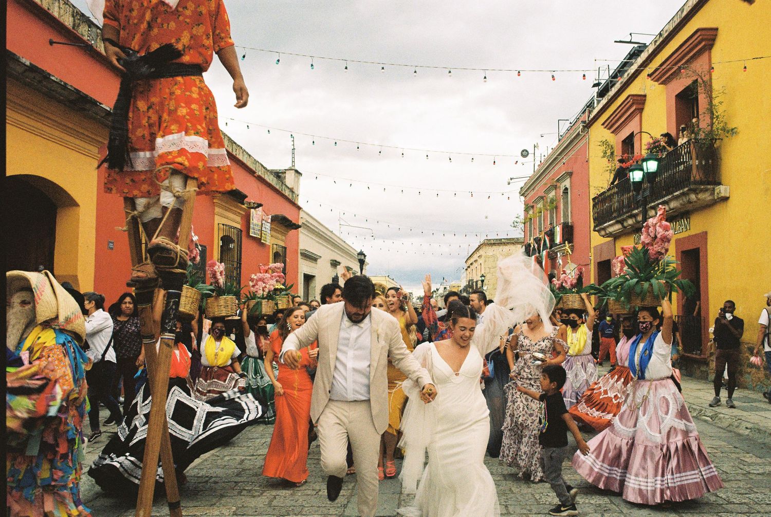 Colorful street parade through historic colonial buildings with string lights overhead.