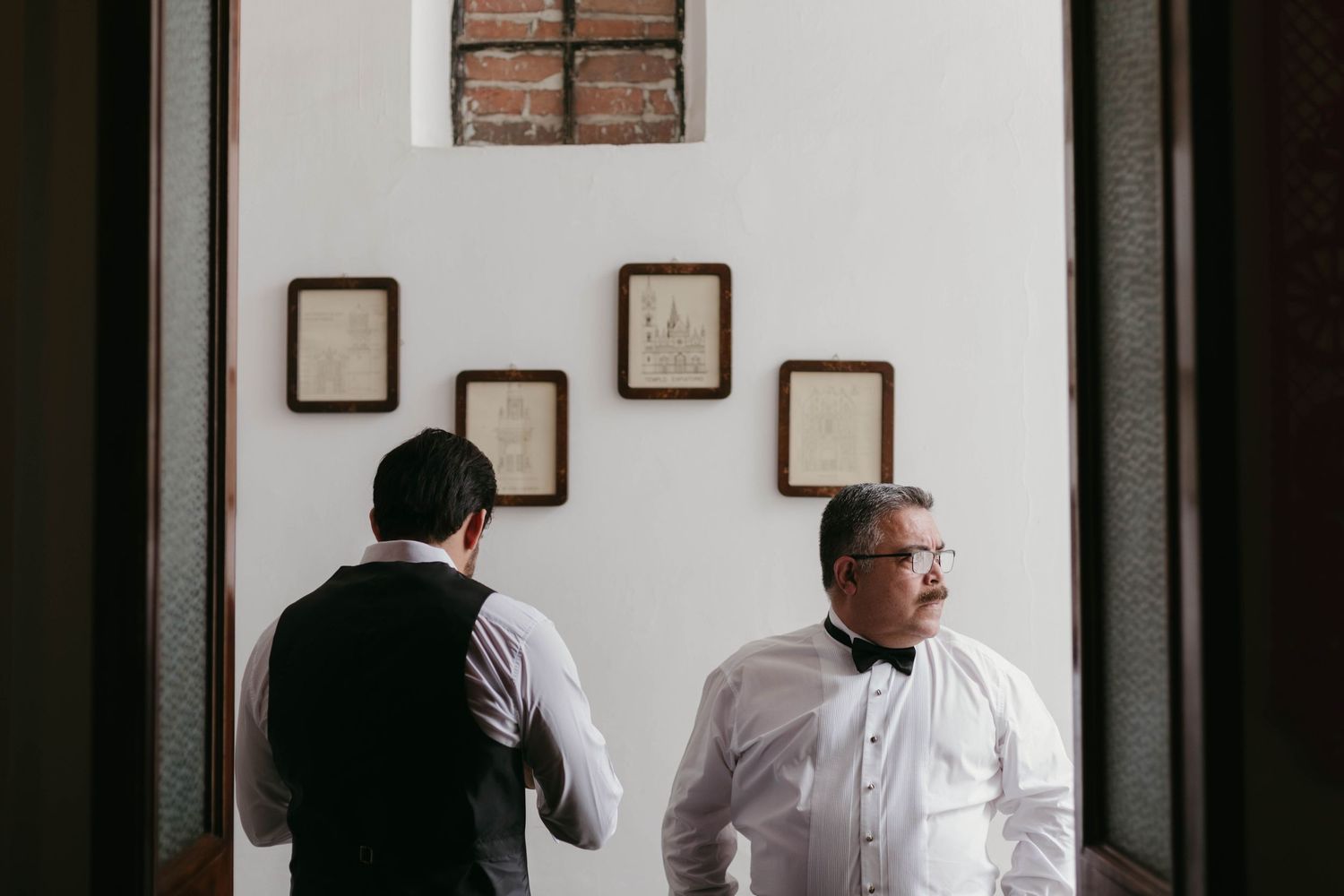 People in formal attire gather in a bright white interior space with dark doorframes.
