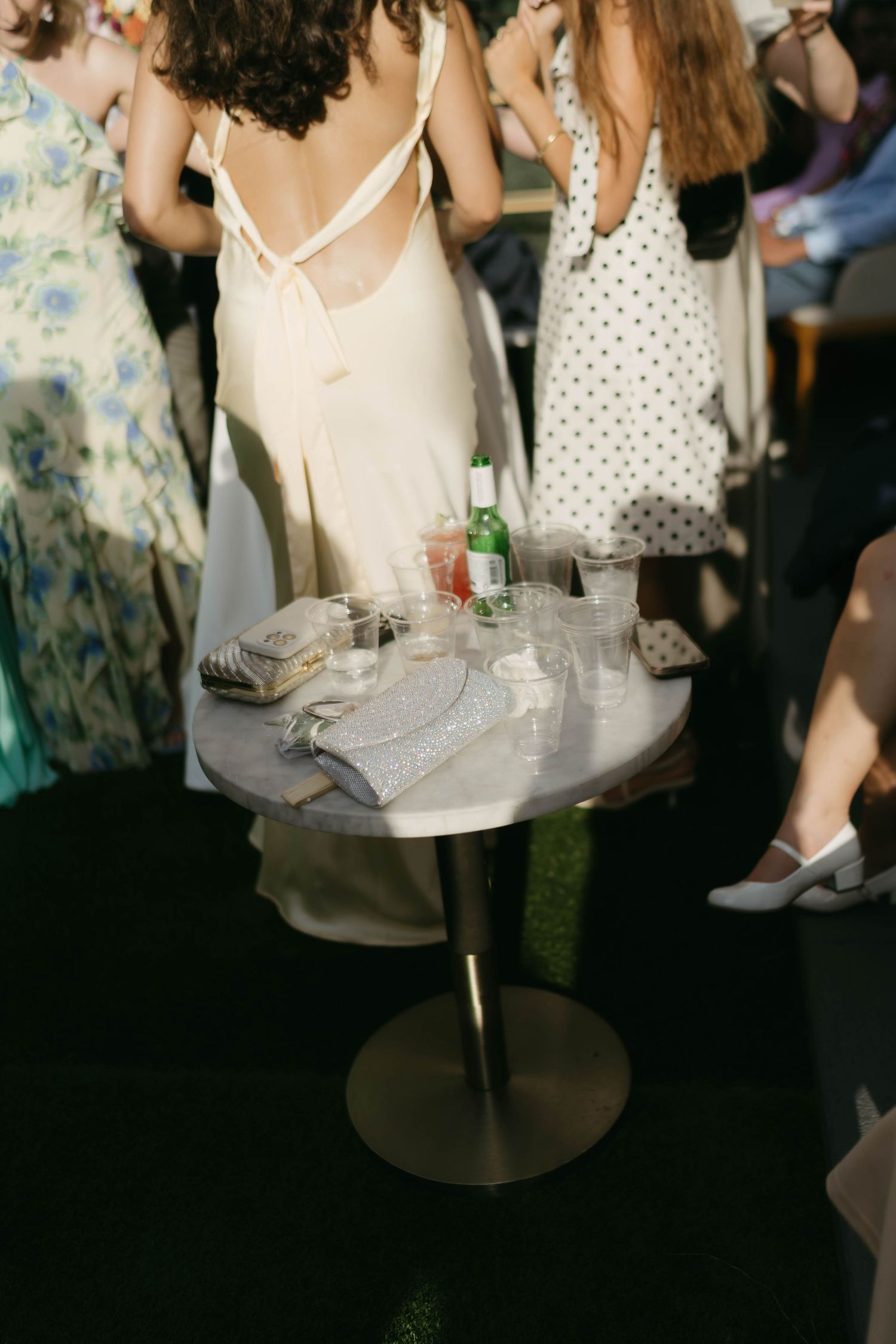 Guests in summer dresses gather around a cocktail table at an outdoor event.
