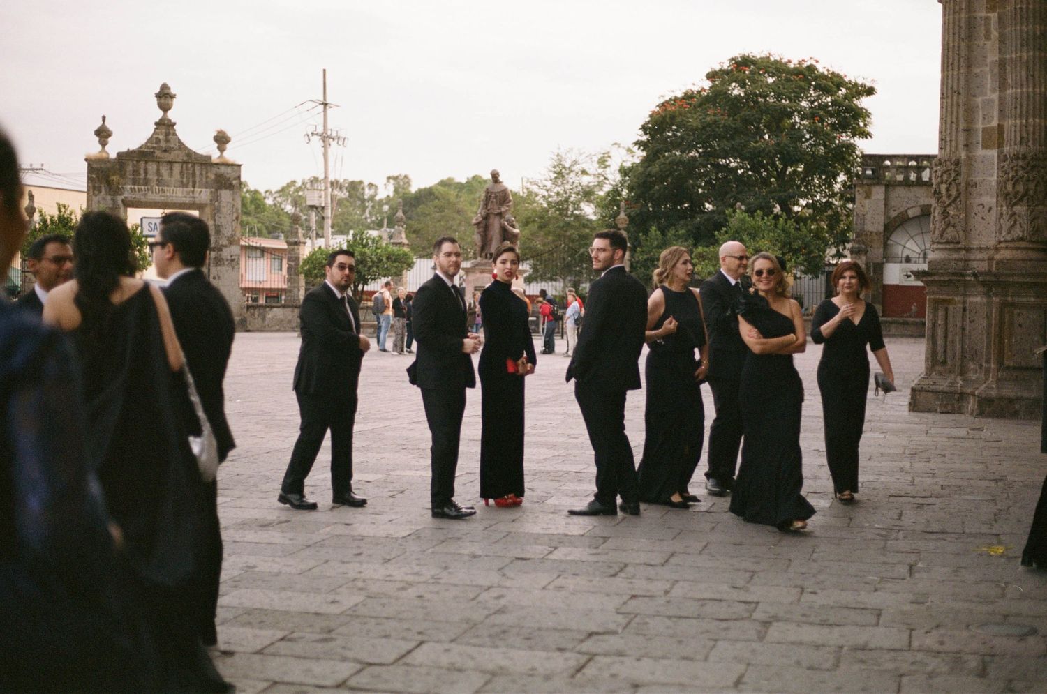 Wedding party and guests gather outside a historic stone building for formal photographs.