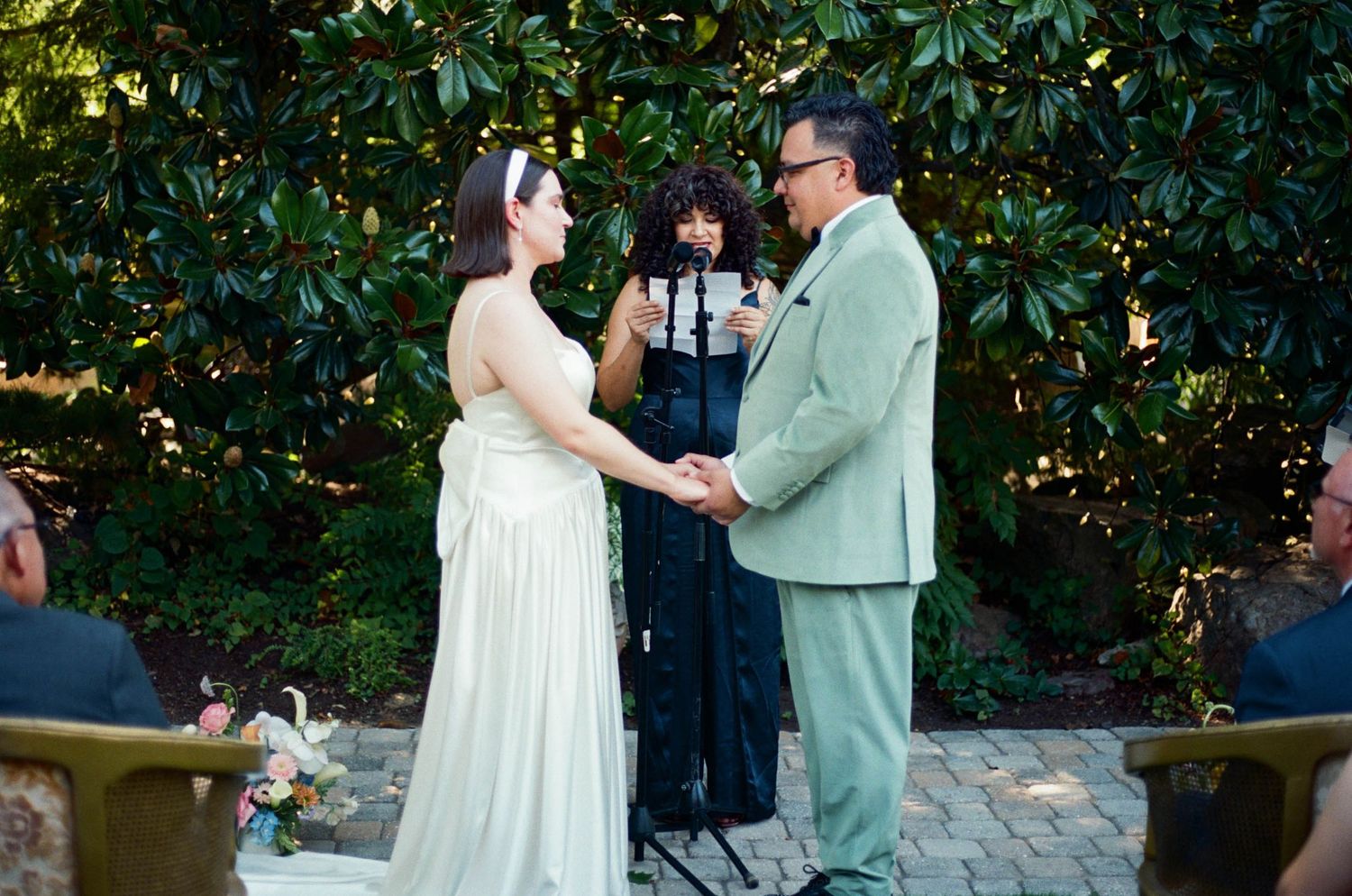 A wedding ceremony takes place on a stone patio surrounded by greenery.