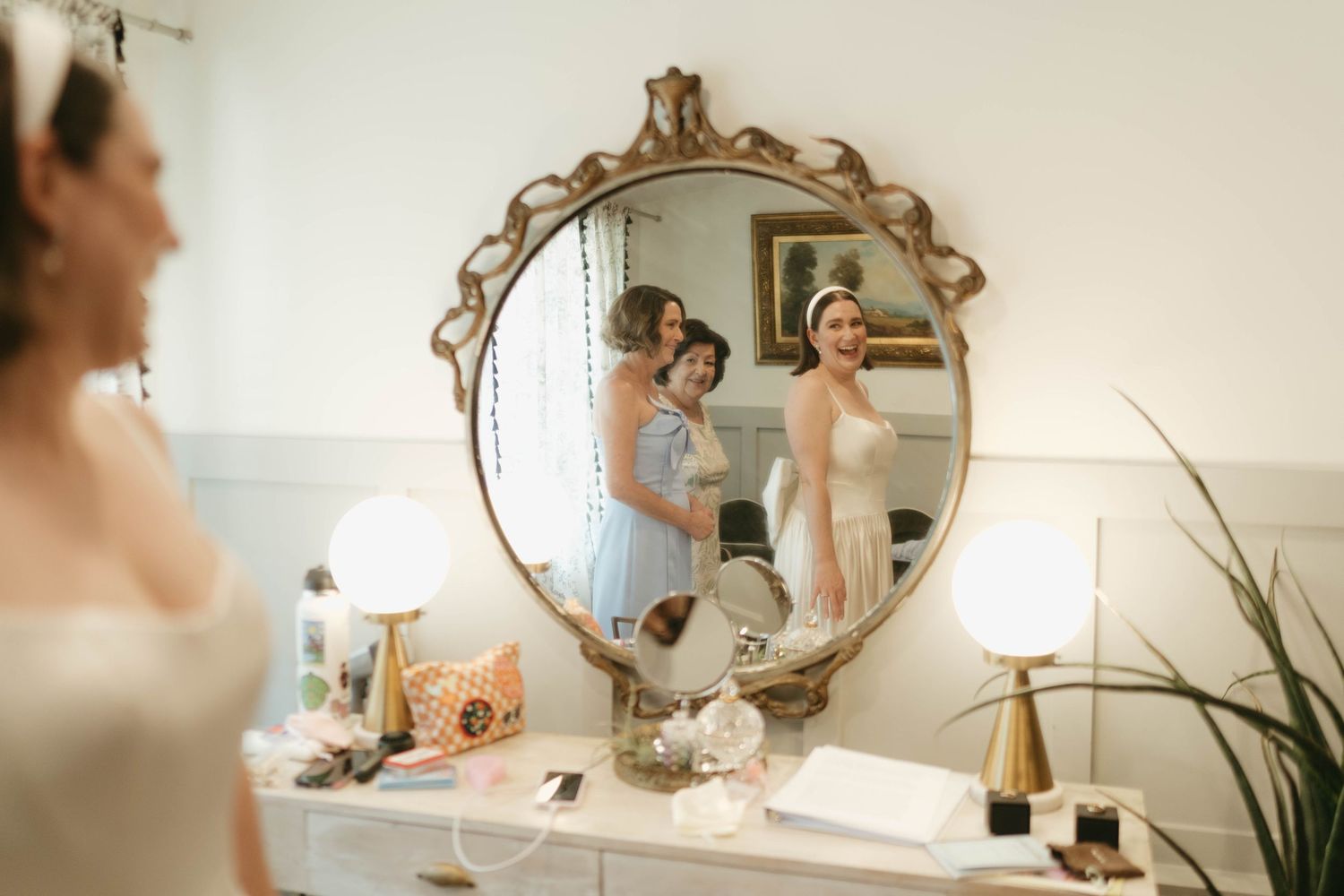 Ornate vintage mirror reflects wedding preparation moments in a softly lit room.