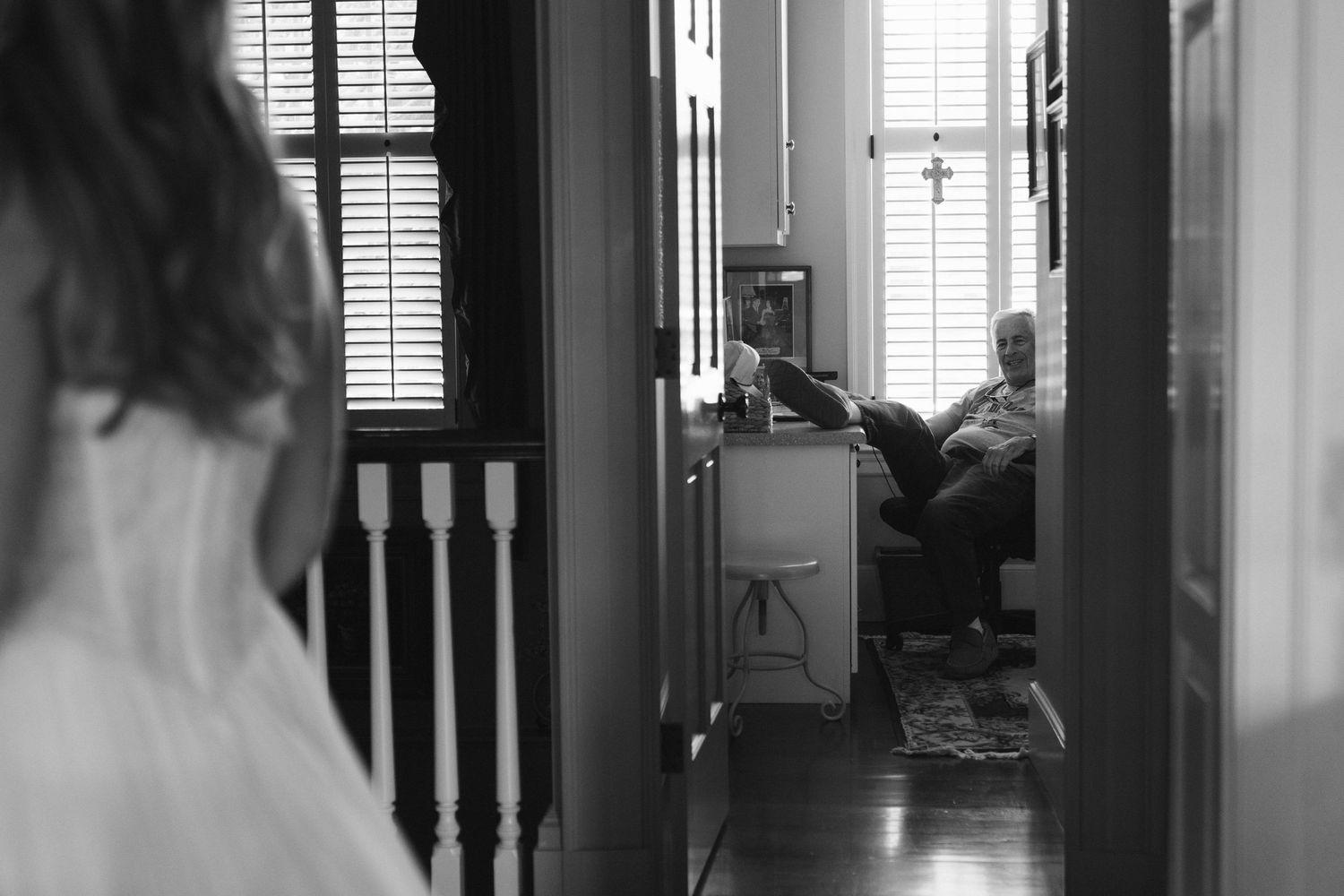 Black and white candid photo of bride in wedding dress glimpsed through doorway of a home interior.