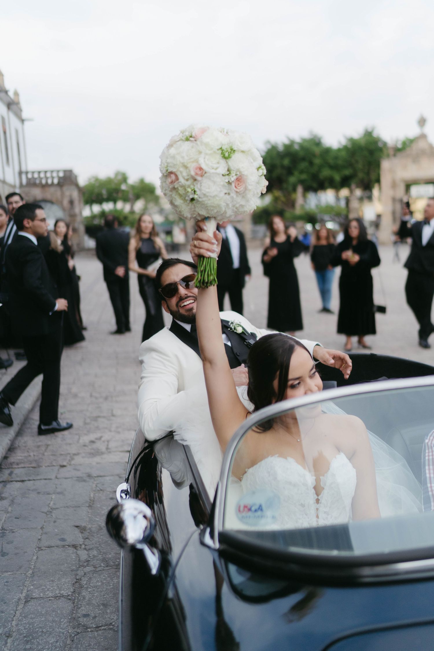Wedding celebration with guests surrounding a vintage convertible car.