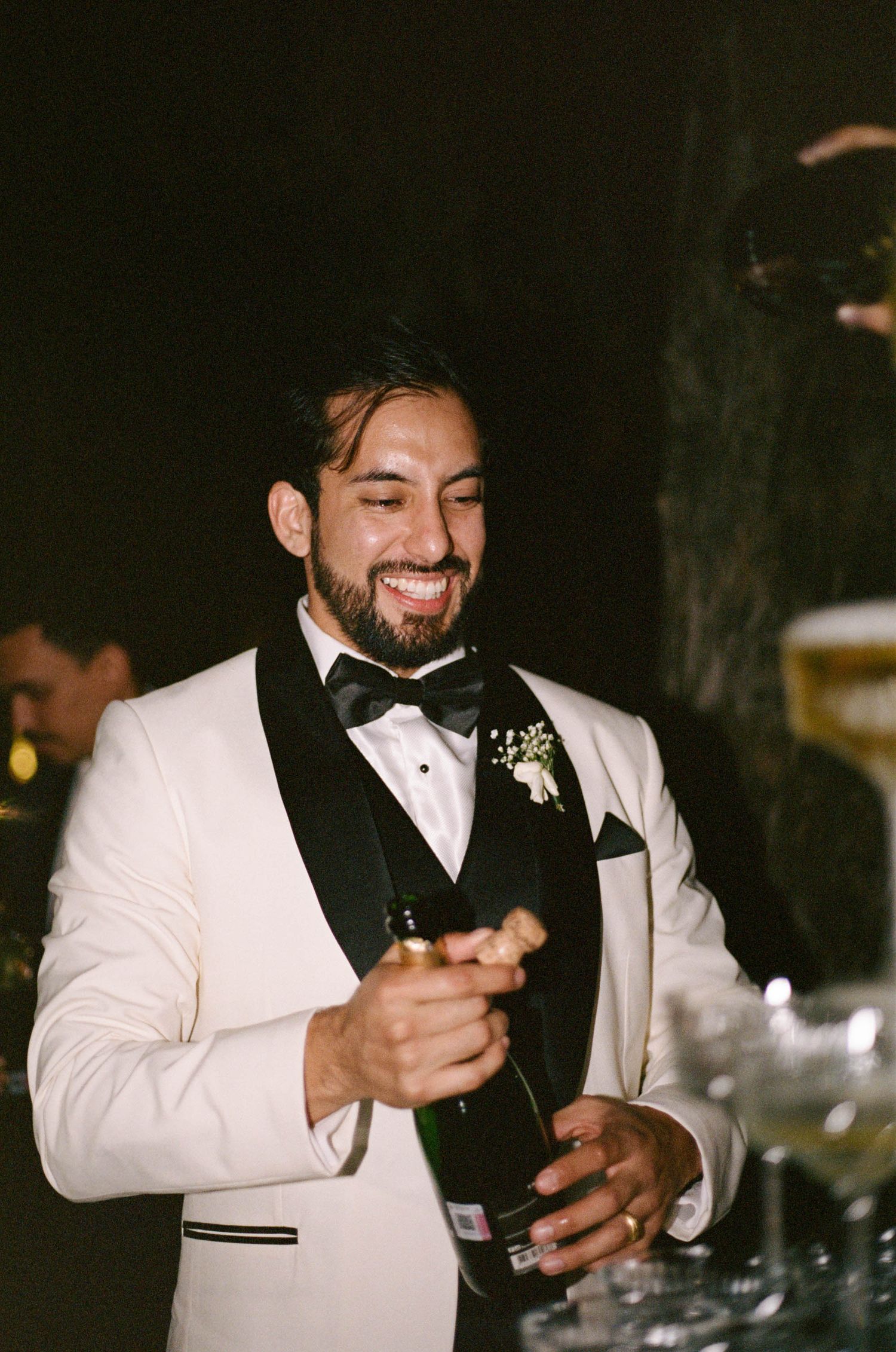 A person in white tuxedo and bow tie smiling during an evening celebration.