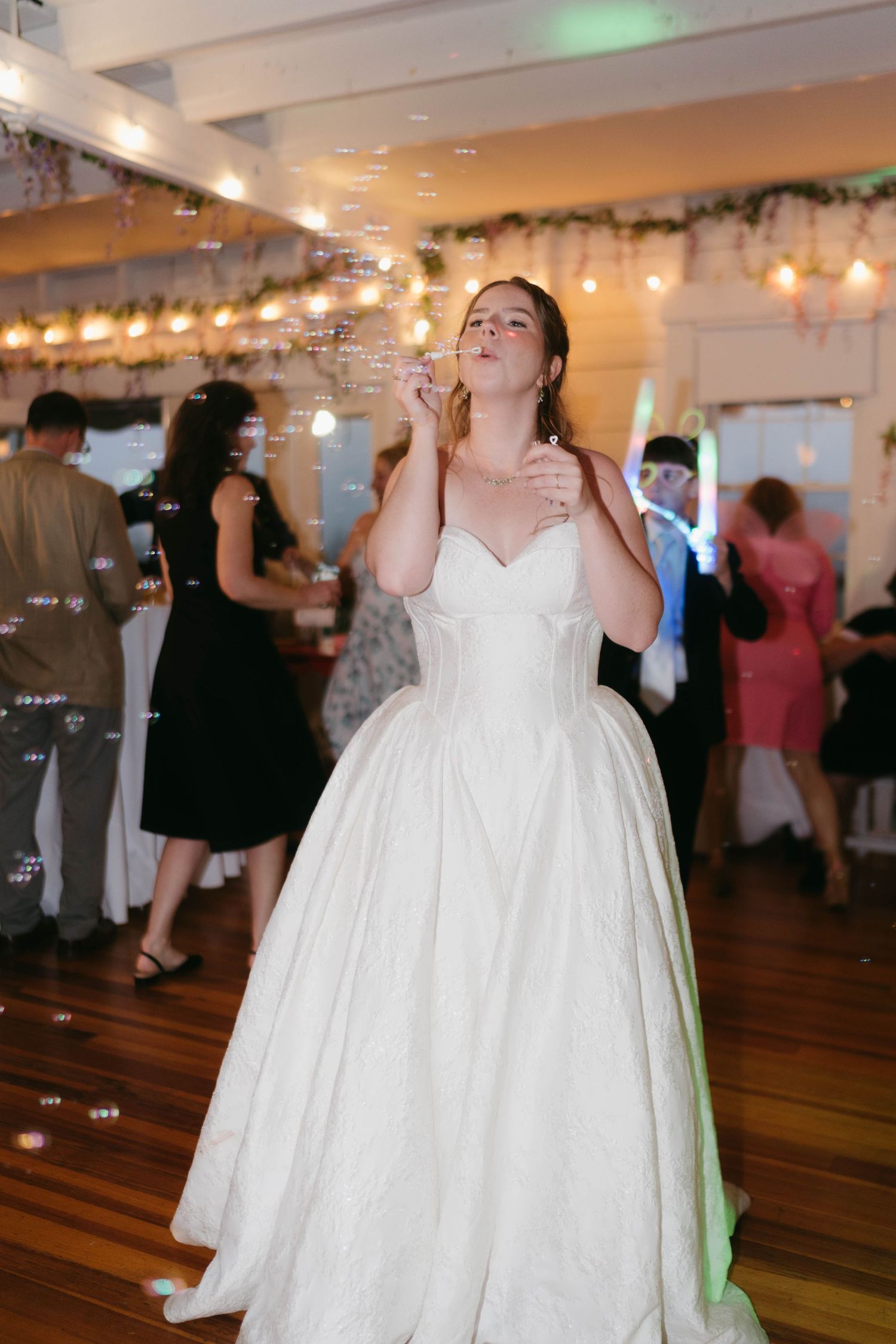 A wedding reception dance floor with guests celebrating under decorative lights and greenery.