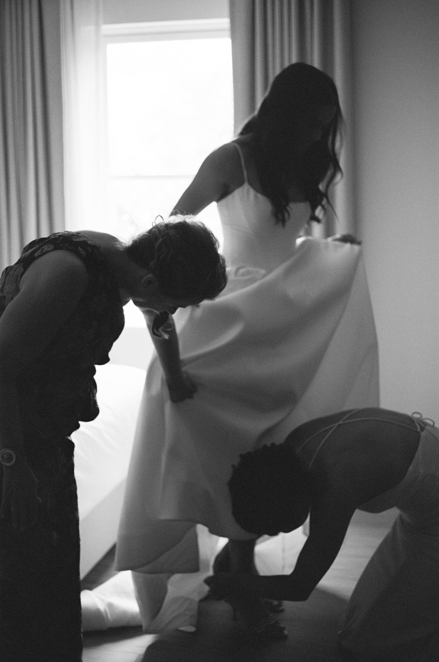 Black and white sequence showing silhouettes preparing a wedding dress near a window.