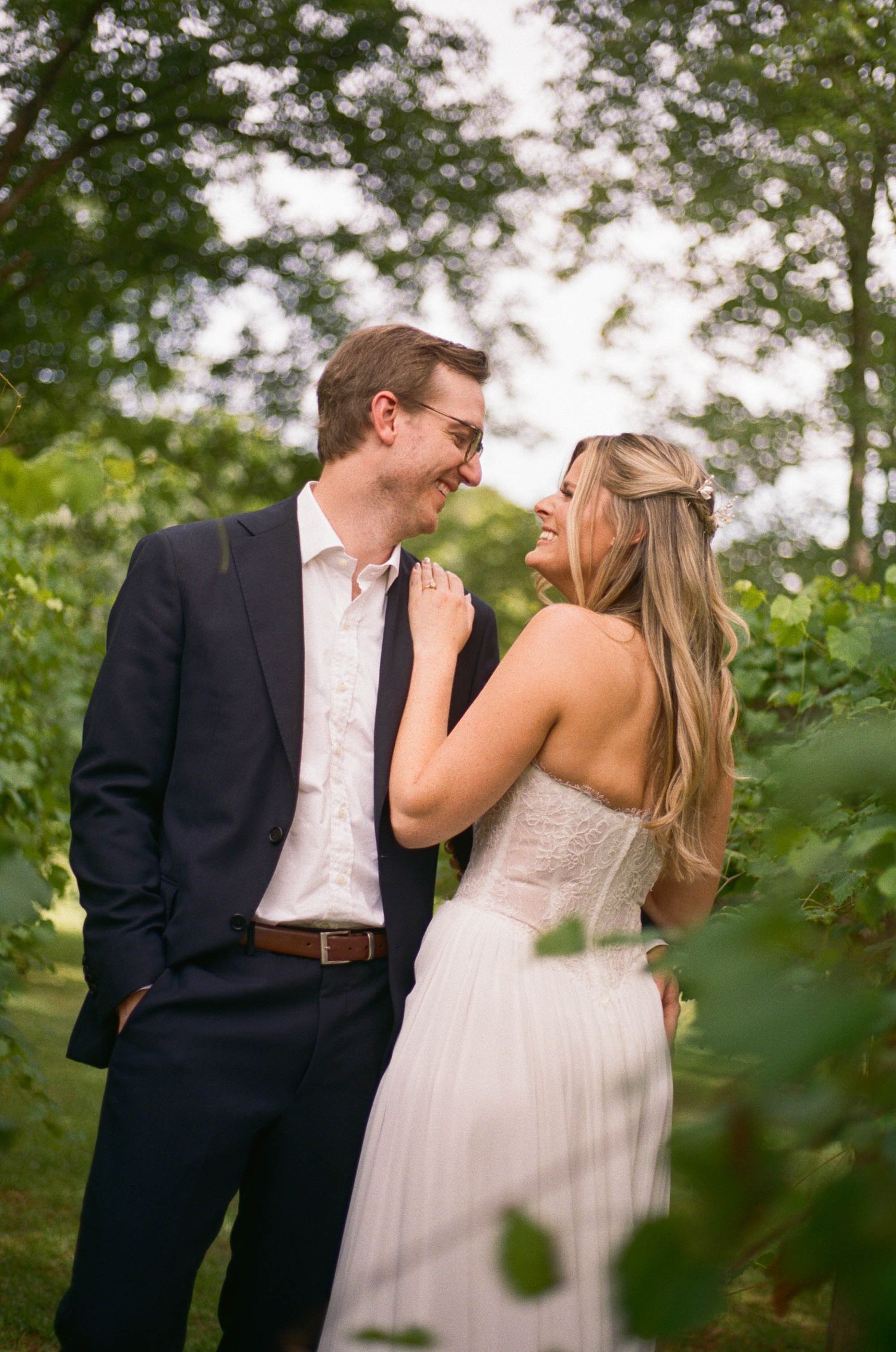 Smiling bride and groom sharing a romantic moment among green foliage in a garden setting.