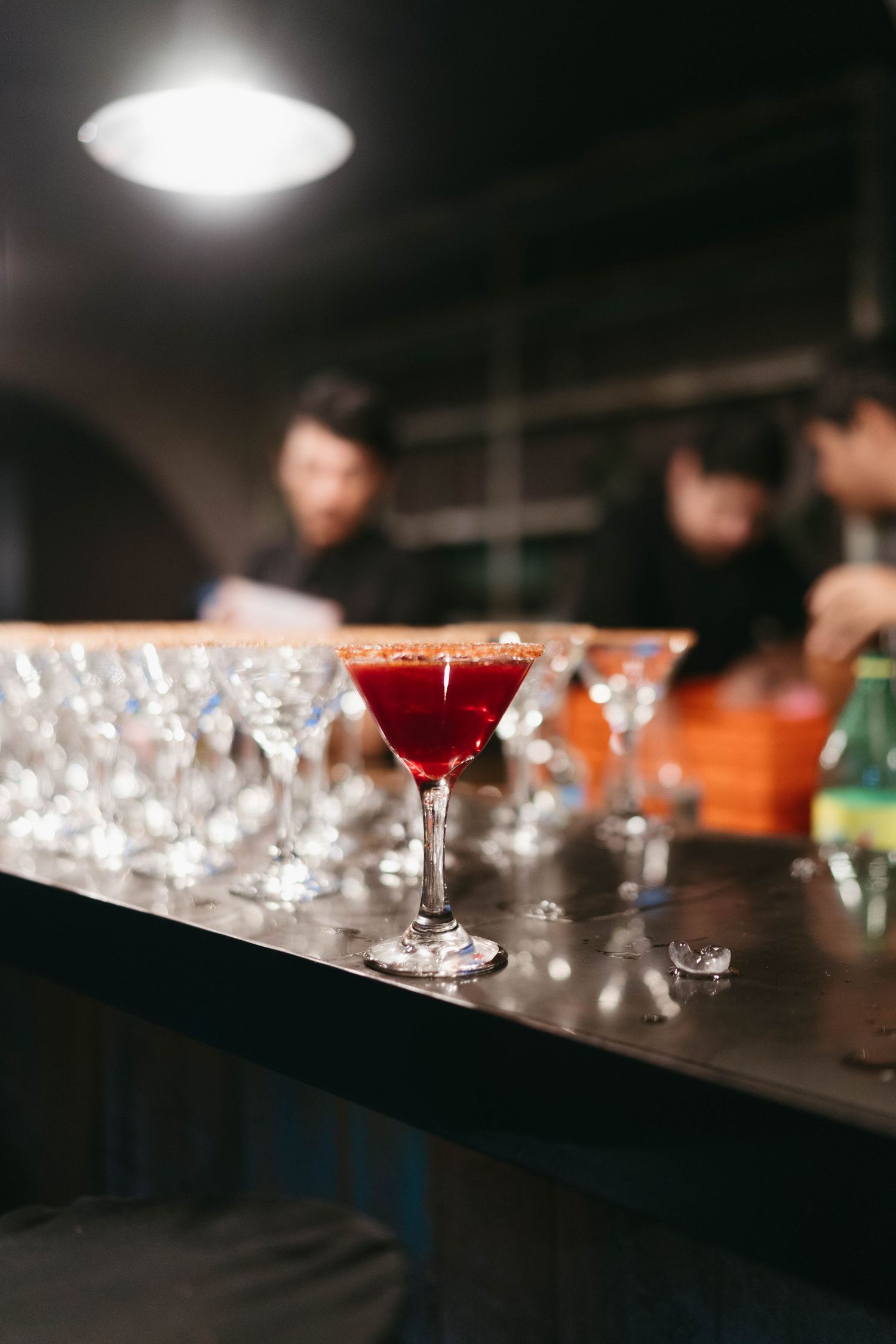 Red cocktails lined up on a dark bar with elegant glassware.