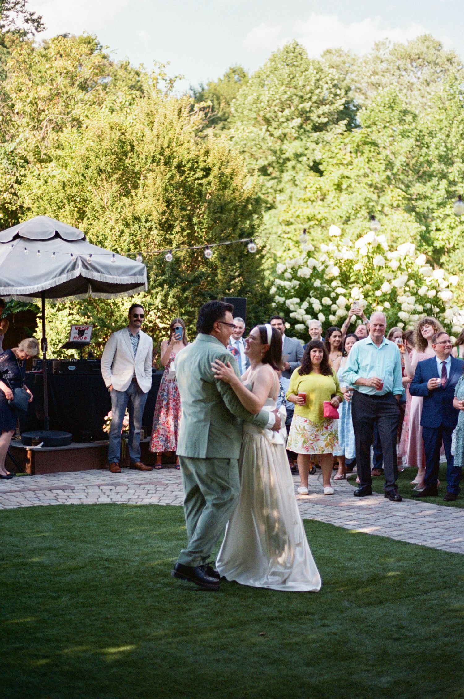Wedding guests watch a couple dancing on a lawn with a gazebo in the background.
