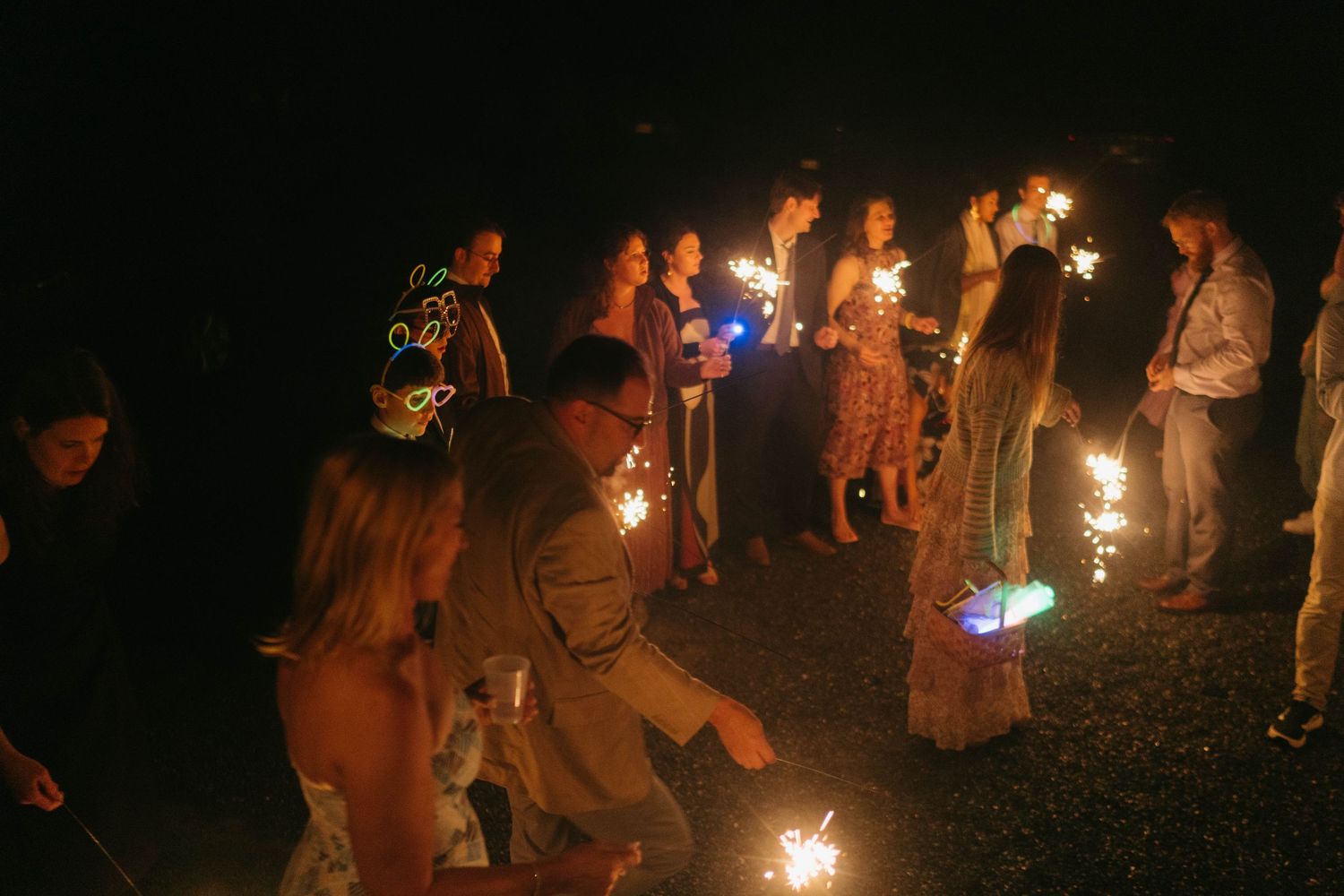 Wedding guests holding sparklers in the dark creating a magical nighttime atmosphere.