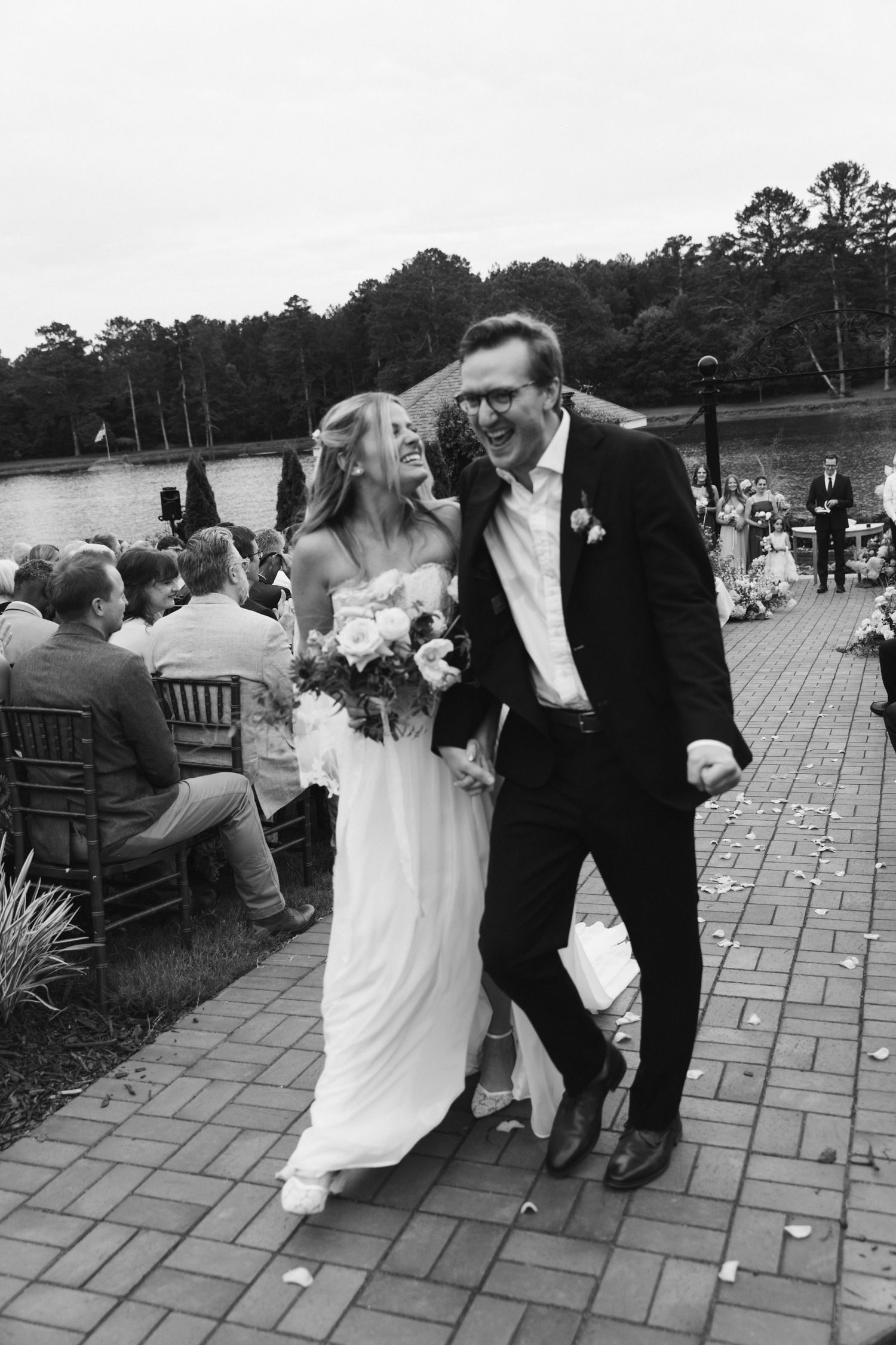 Black and white photo of joyful newlyweds walking down the aisle after their outdoor waterfront wedding ceremony.